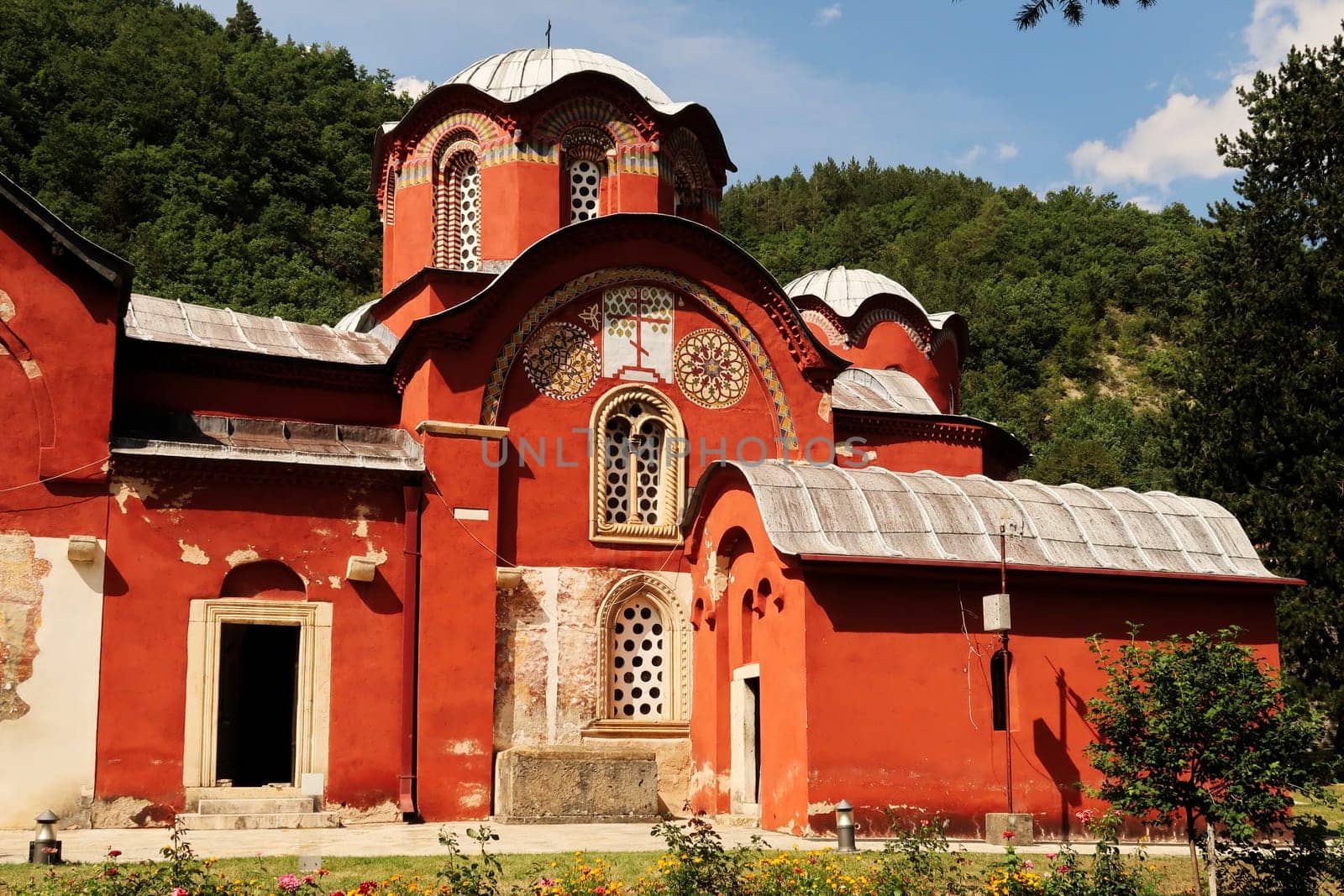 The elaborate front facade and roof with domes, cupolas of the bright red Church Complex inside the courtyard, garden of the Patriarchate of Pec Monastery, outside of Peja, Kosovo 2022