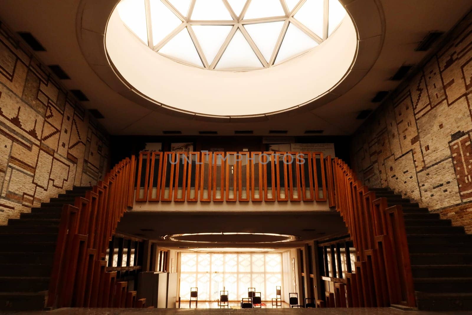Light is shining throug a big dome with geometric pattern onto the stairs, staircase, hallway with wooden rails, handrails, railings inside the National University Library of Kosovo, Prishtina, Pristina, Kosovo, 25th of July 2022
