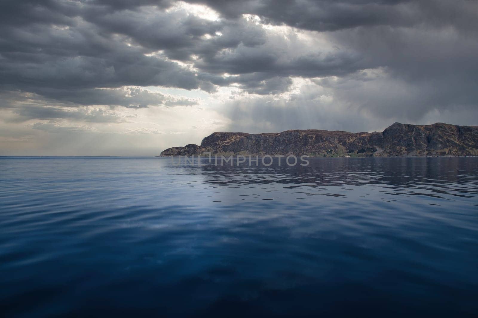 View from the sea to the West Cape in Norway under a dramatic sky. Waves in the foreground, rocks in the background. Westernmost point of the Eu