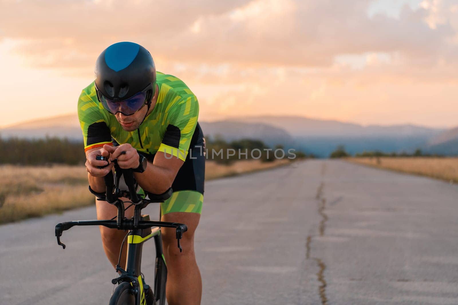 Triathlete riding his bicycle during sunset, preparing for a marathon. The warm colors of the sky provide a beautiful backdrop for his determined and focused effort