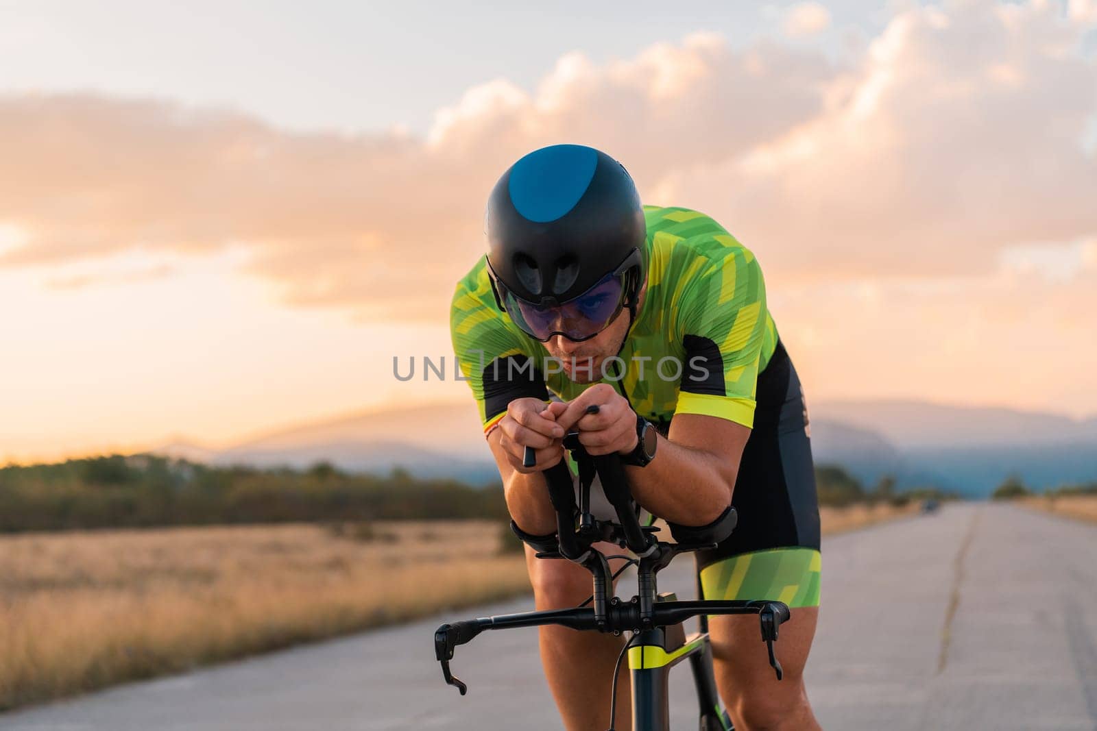 Triathlete riding his bicycle during sunset, preparing for a marathon. The warm colors of the sky provide a beautiful backdrop for his determined and focused effort