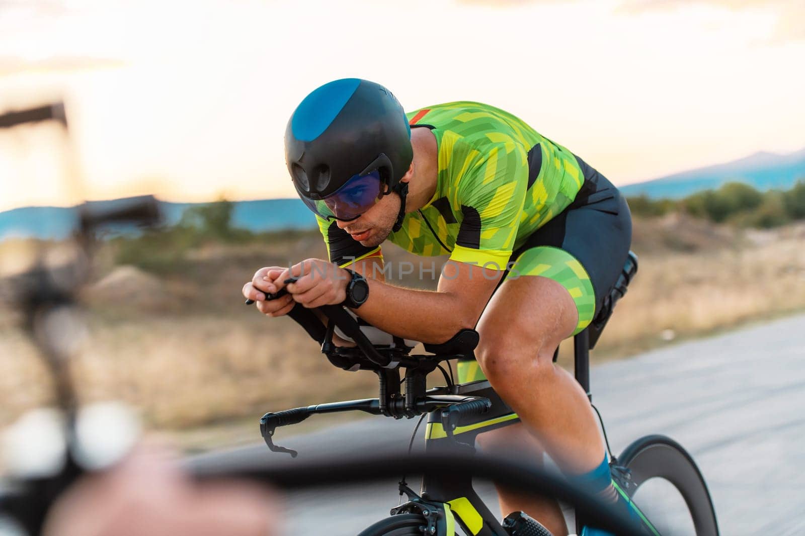 Triathlete riding his bicycle during sunset, preparing for a marathon. The warm colors of the sky provide a beautiful backdrop for his determined and focused effort