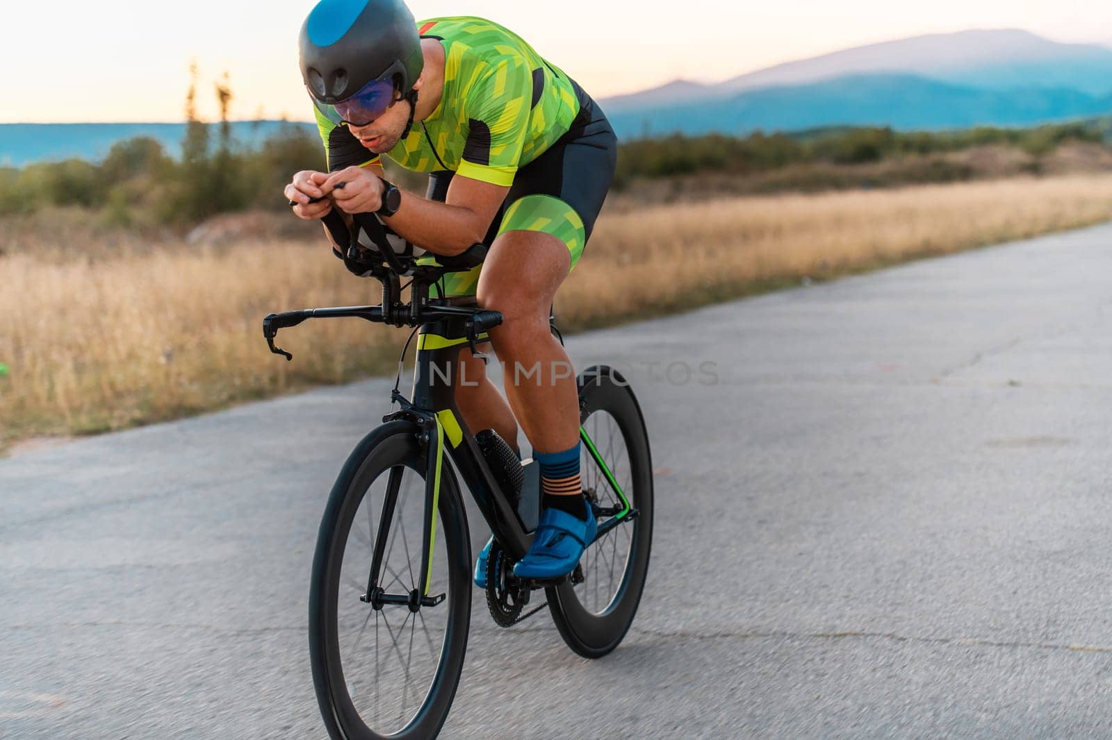 Triathlete riding his bicycle during sunset, preparing for a marathon. The warm colors of the sky provide a beautiful backdrop for his determined and focused effort