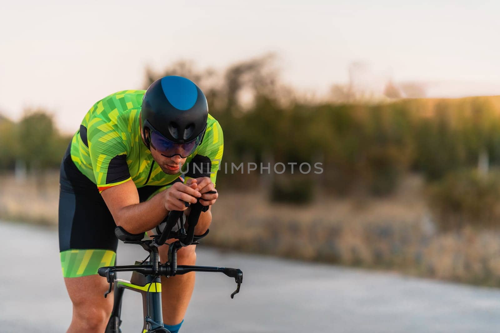 Triathlete riding his bicycle during sunset, preparing for a marathon. The warm colors of the sky provide a beautiful backdrop for his determined and focused effort
