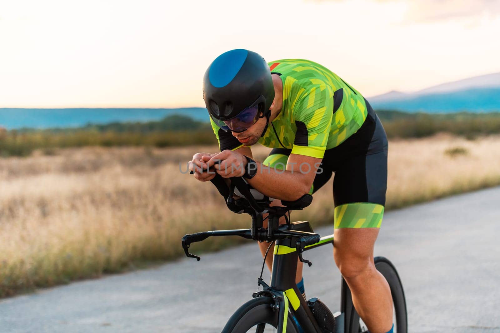Triathlete riding his bicycle during sunset, preparing for a marathon. The warm colors of the sky provide a beautiful backdrop for his determined and focused effort