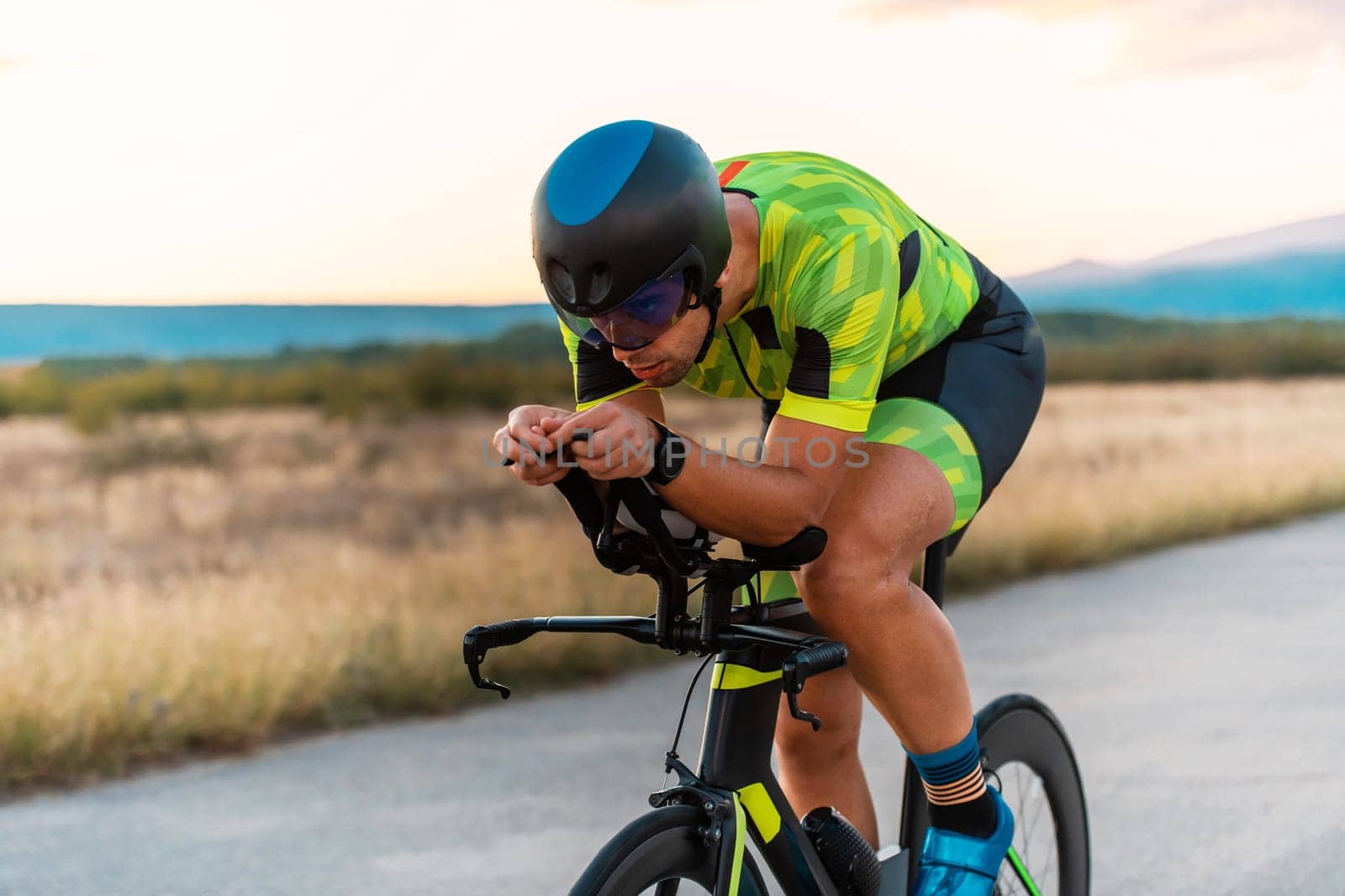 Close up photo of triathlete riding his bicycle during sunset, preparing for a marathon. The warm colors of the sky provide a beautiful backdrop for his determined and focused effort