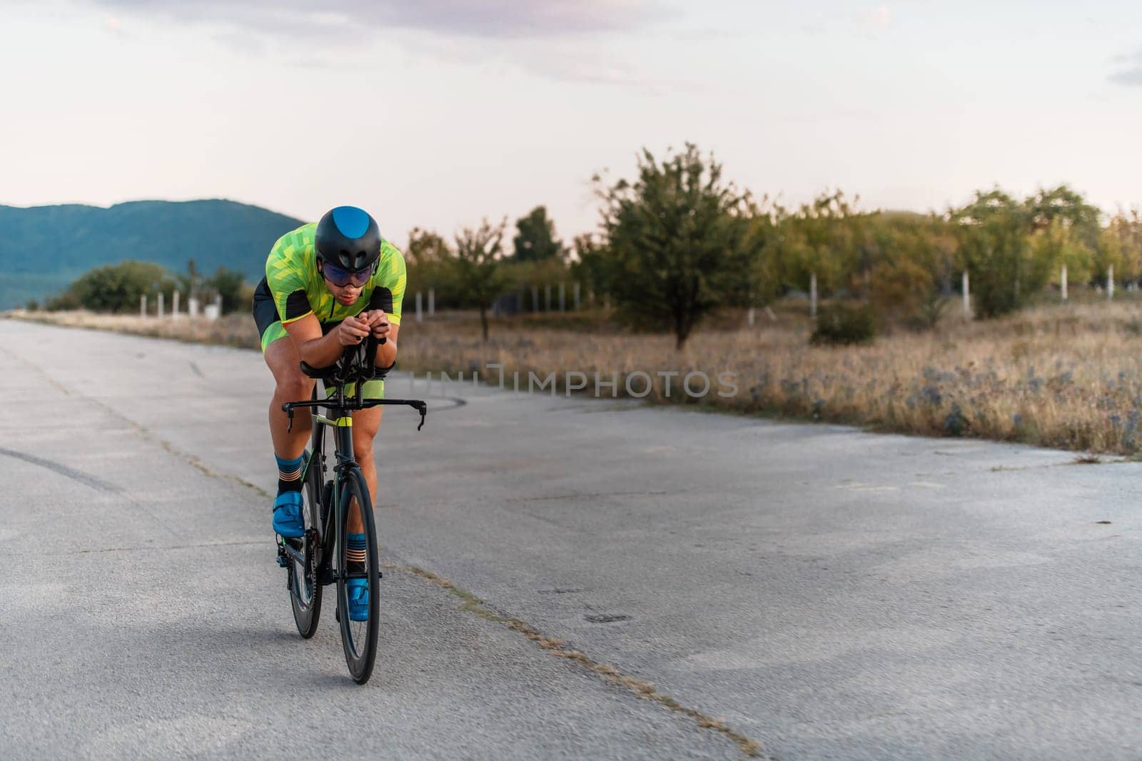 Triathlete riding his bicycle during sunset, preparing for a marathon. The warm colors of the sky provide a beautiful backdrop for his determined and focused effort