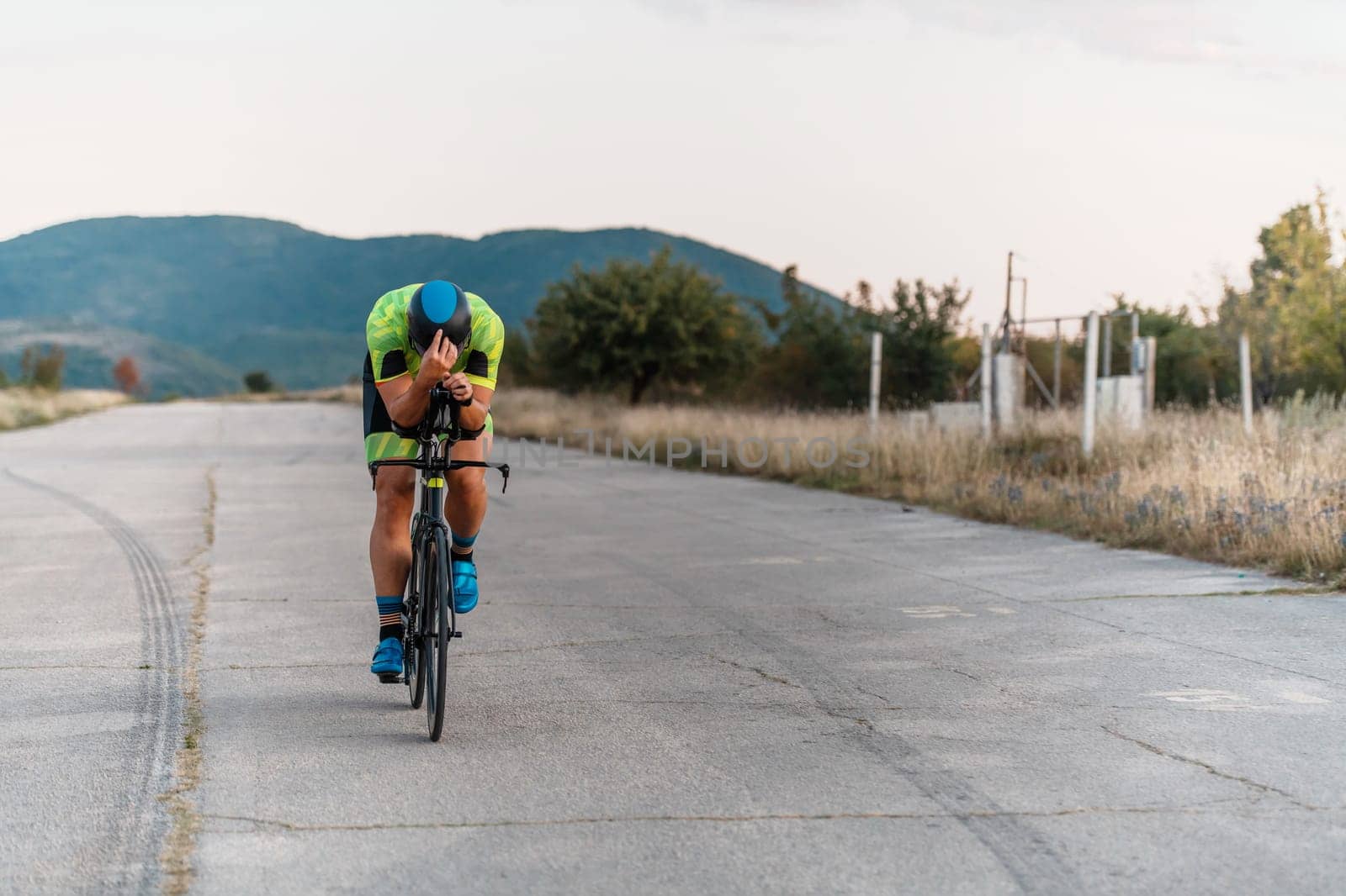 Triathlete riding his bicycle during sunset, preparing for a marathon. The warm colors of the sky provide a beautiful backdrop for his determined and focused effort