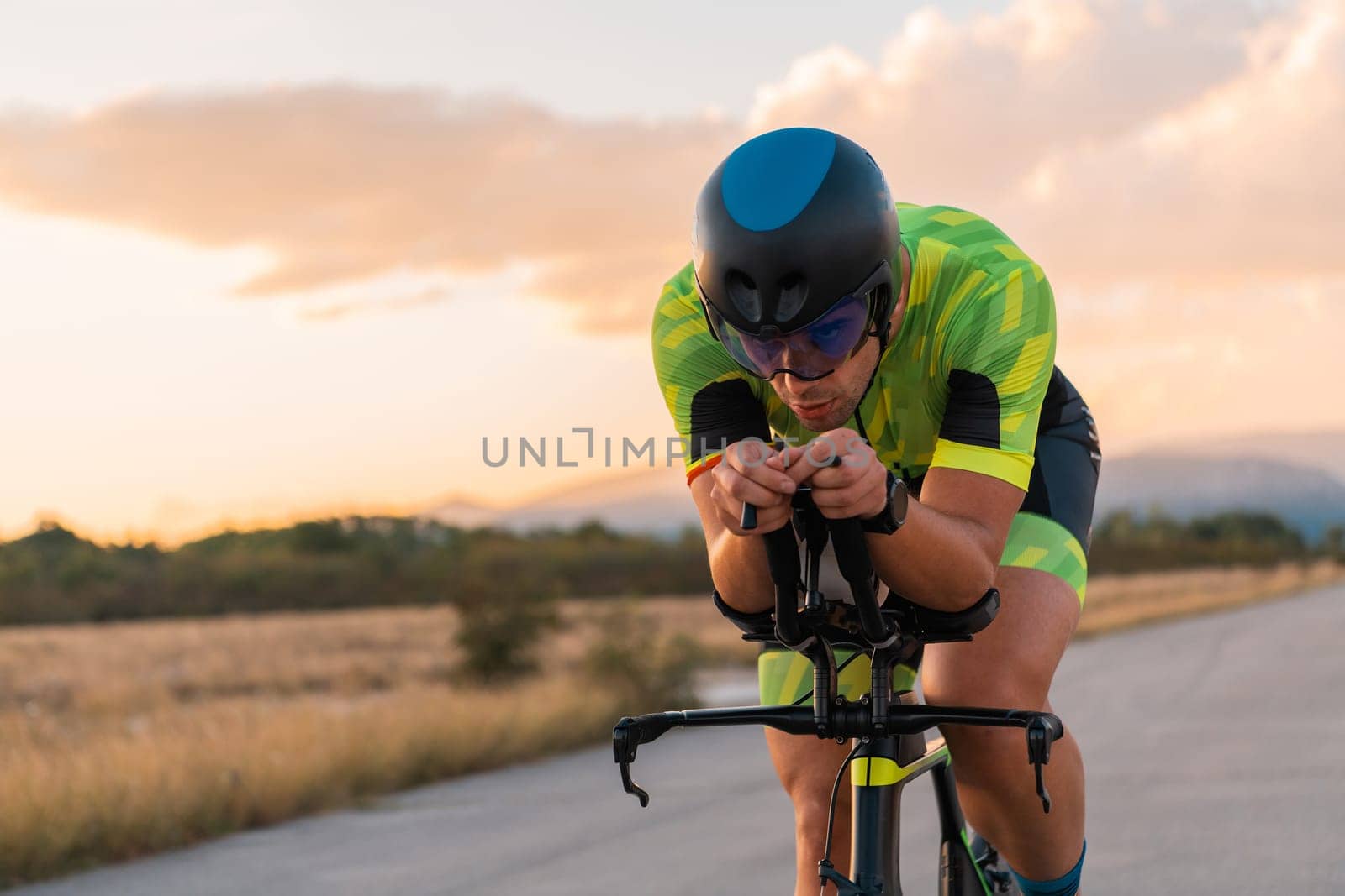 Triathlete riding his bicycle during sunset, preparing for a marathon. The warm colors of the sky provide a beautiful backdrop for his determined and focused effort