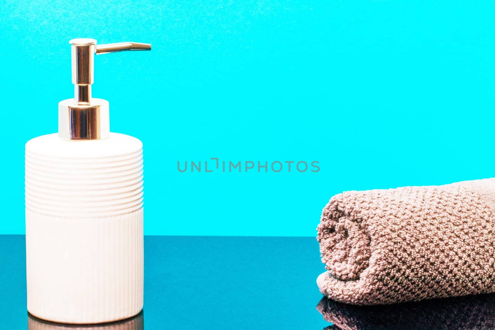 Macro of a beauty cosmetic makeup bottle and a fresh soft terry bath towel on dark table over blue background. Copy space for product display montage.