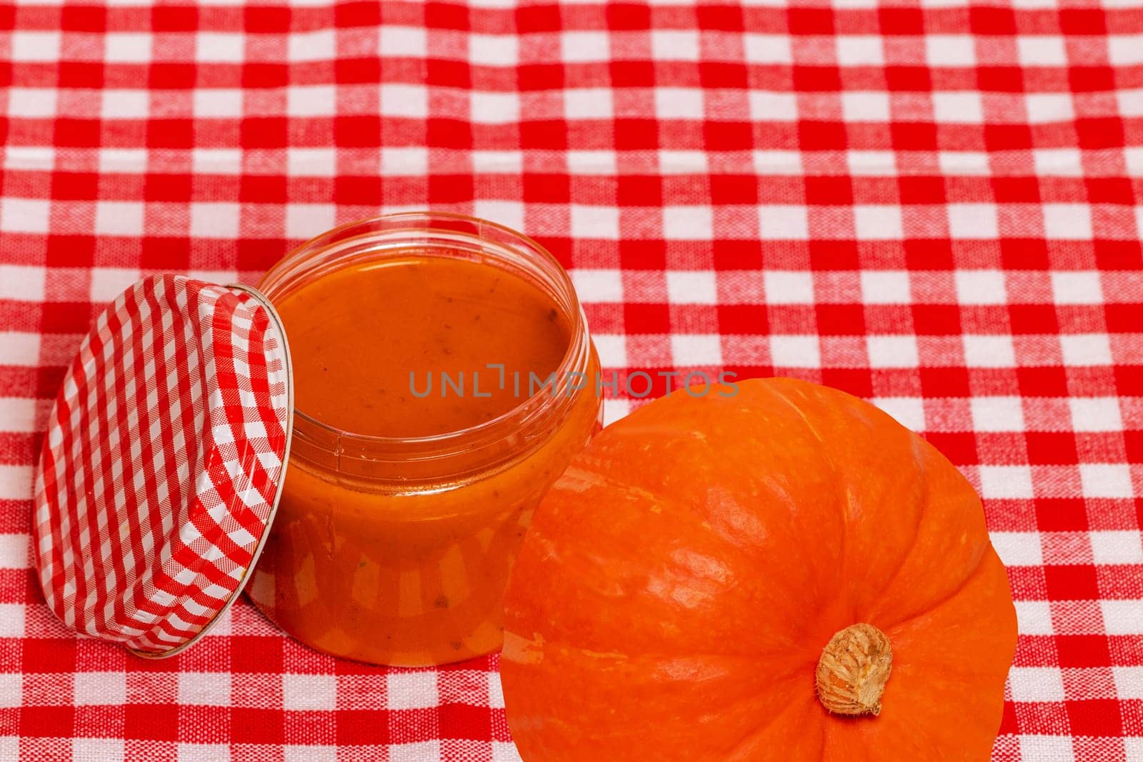 Natural cosmetics. Selective focus on a homemade pumpkin face mask in a glass jar and pumpkins on red checkered napkin. DIY cosmetics and SPA. Copy space.