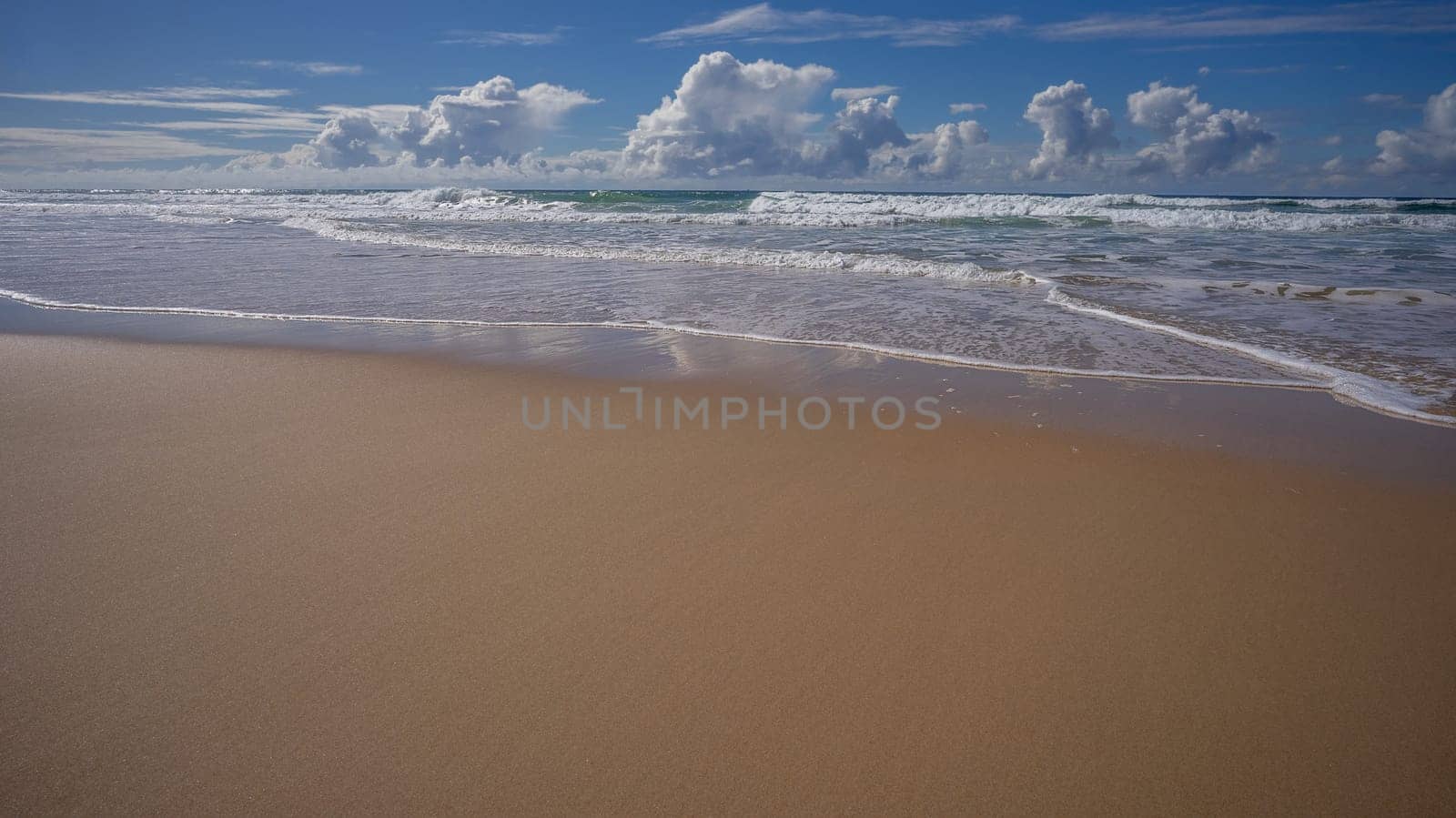 A beach scene with copy space for tourism with sand surf waves clouds blue sky in winter Queensland Australia