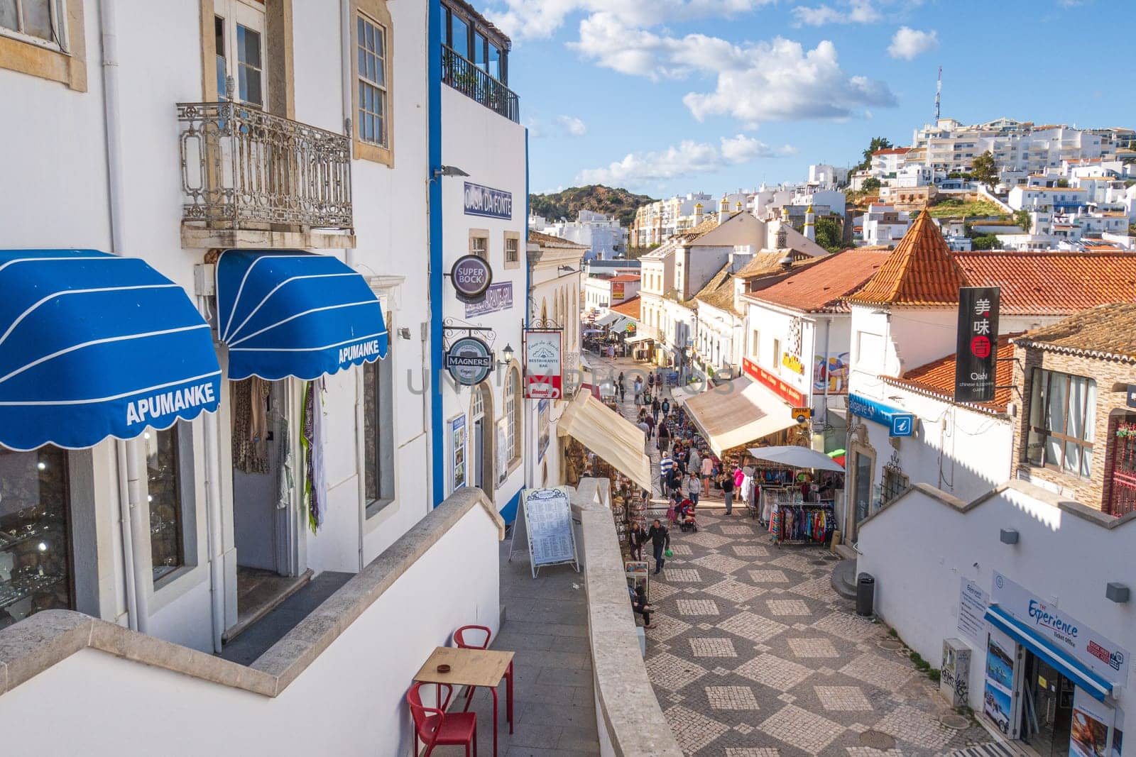 Albufeira, Portugal - April 27, 2024: traditional buildings and tourists photographed in a street of  Albufeira at the Algarve coast of Portugal