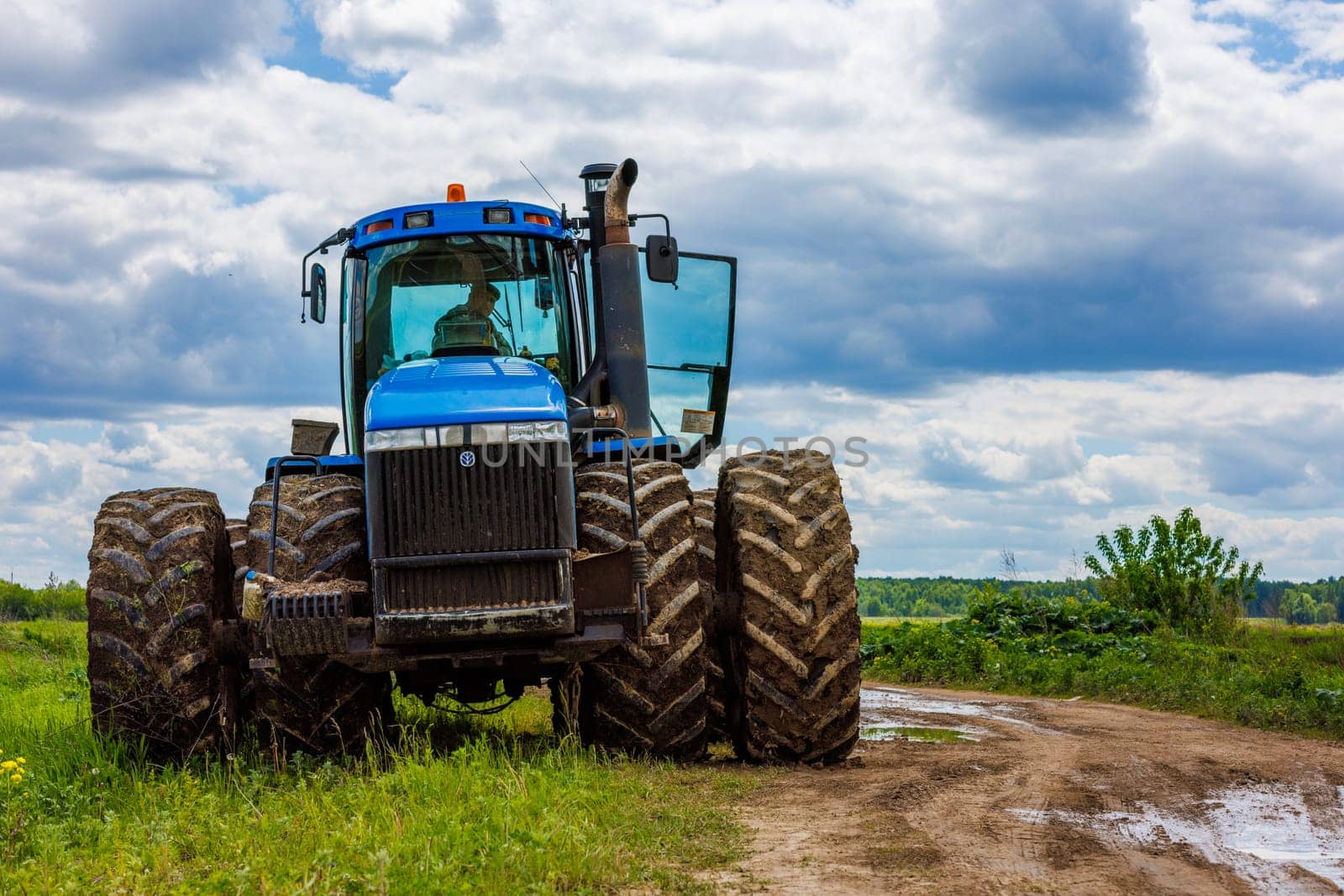 Blue New Holland tractor with double wheels standing near agricultural field at hot sunny day in Tula, Russia - June 4, 2022