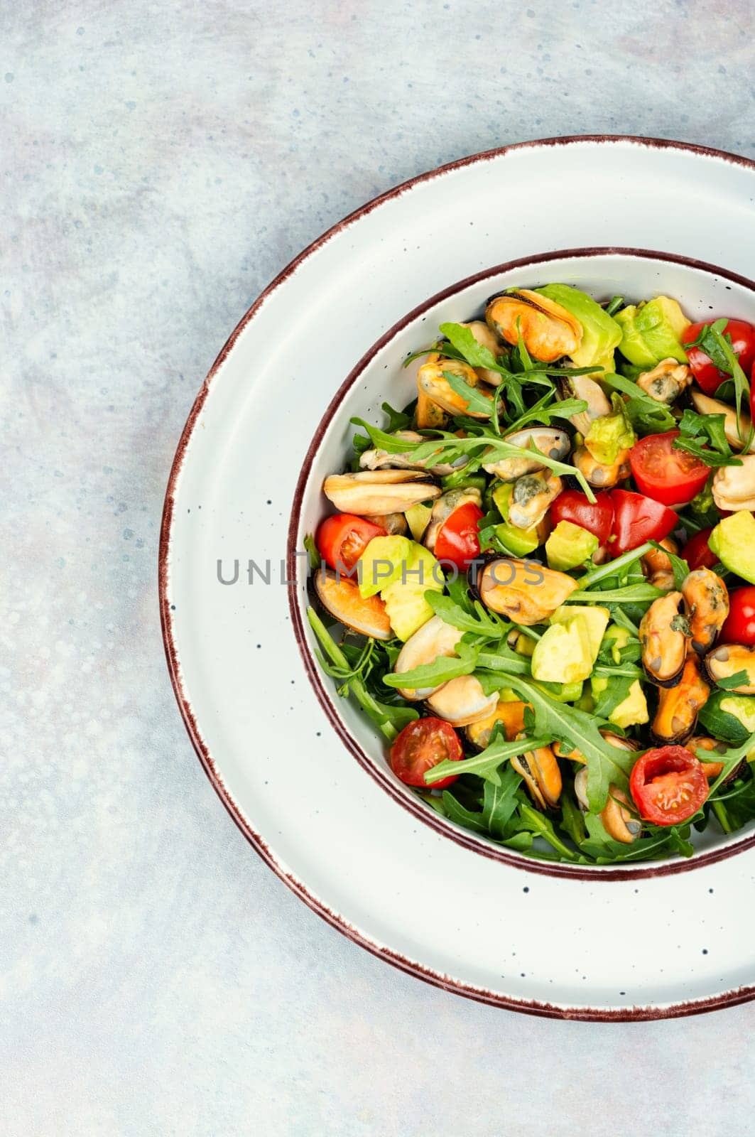 Plate with vitamin salad of mussels, arugula, tomato and avocado. Top view.