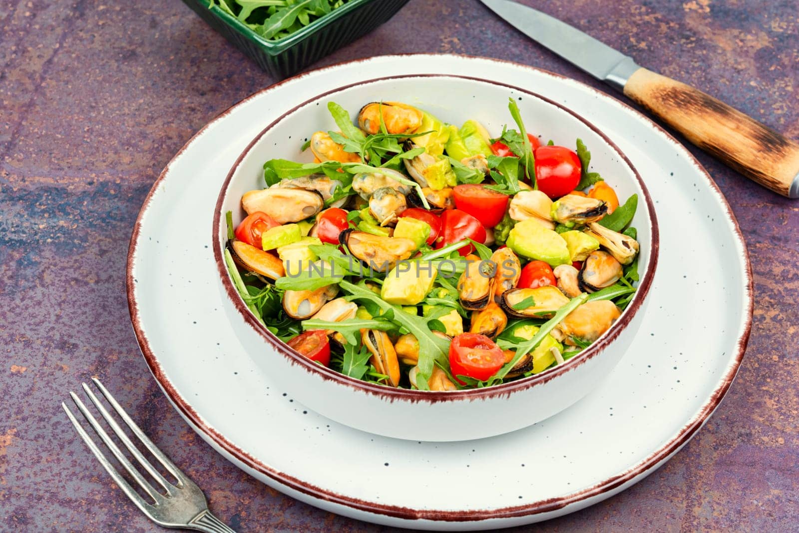 Plate with vitamin salad of mussels, arugula, tomato and avocado. Top view.