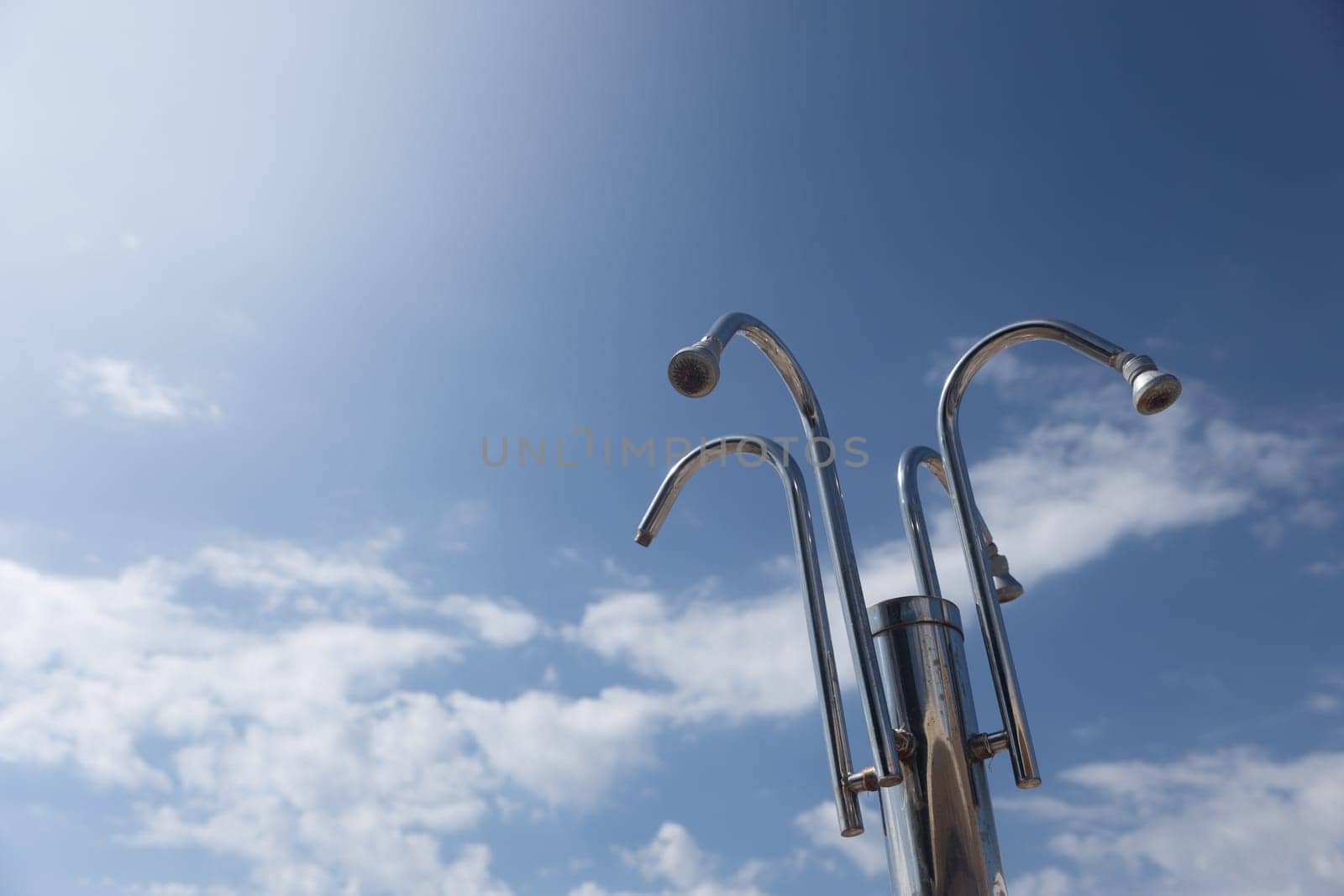 Beach Shower Heads Against Blue Sky. Group of metal shower heads standing high against a blue sky with scattered clouds. Copy space.High quality photo