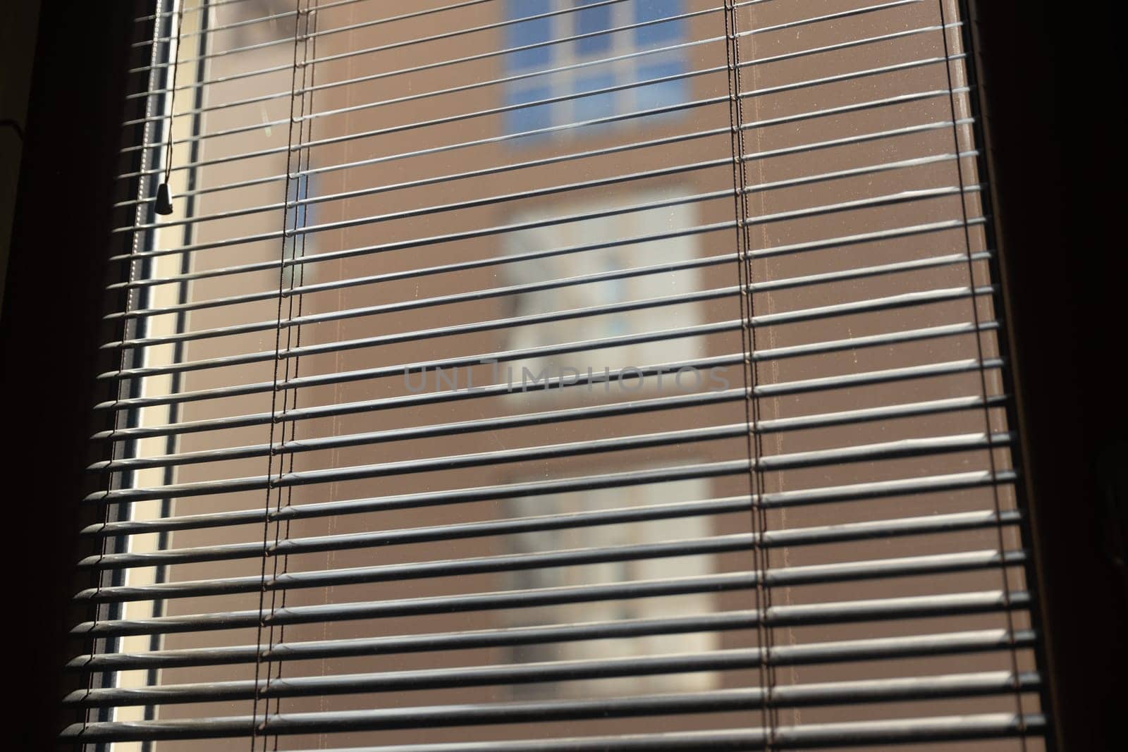 Close-up of partially open blinds revealing a blurred view of the building's exterior. The horizontal lines of the blinds create a repeating pattern. Copy space. High quality photo