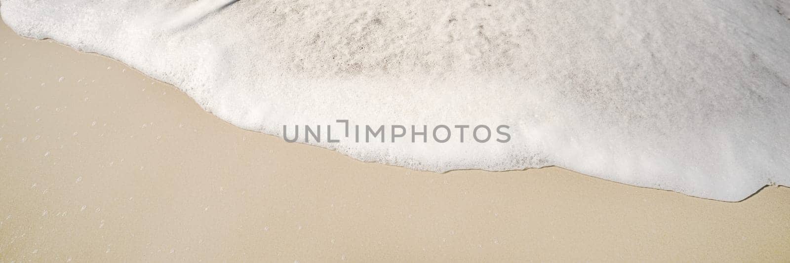 White fluffy foam from a wave breaking rolling onto the sandy beach background image