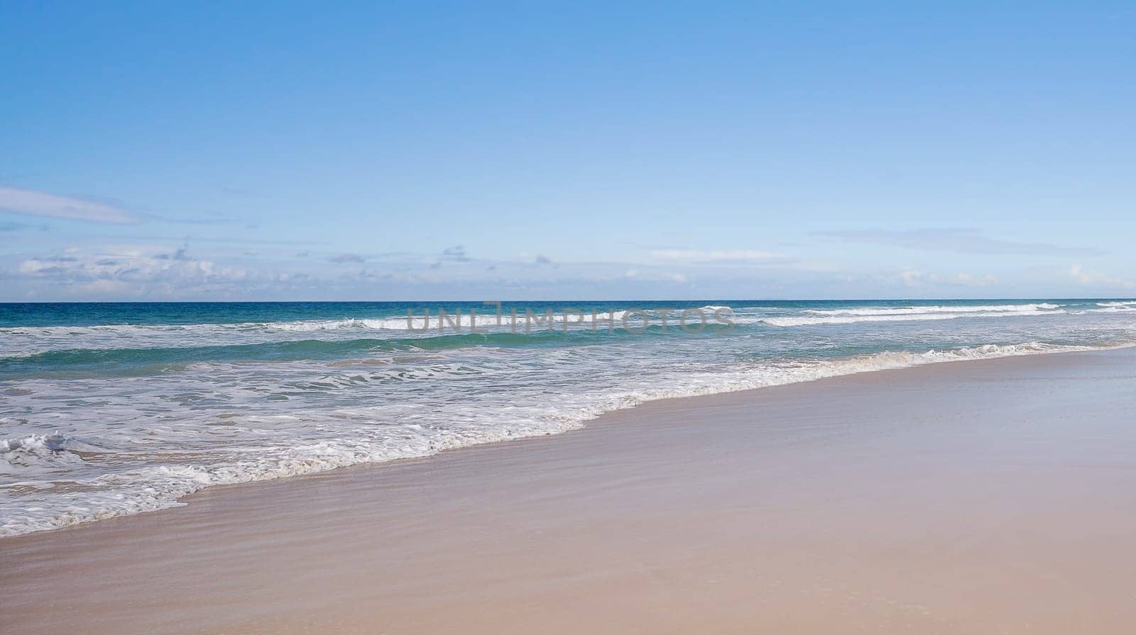 Panoramic beach scene with wet smooth sand, sea, breaking waves, horizon and blue sky and copyspace, blank space with no landmarks, nobody, no people