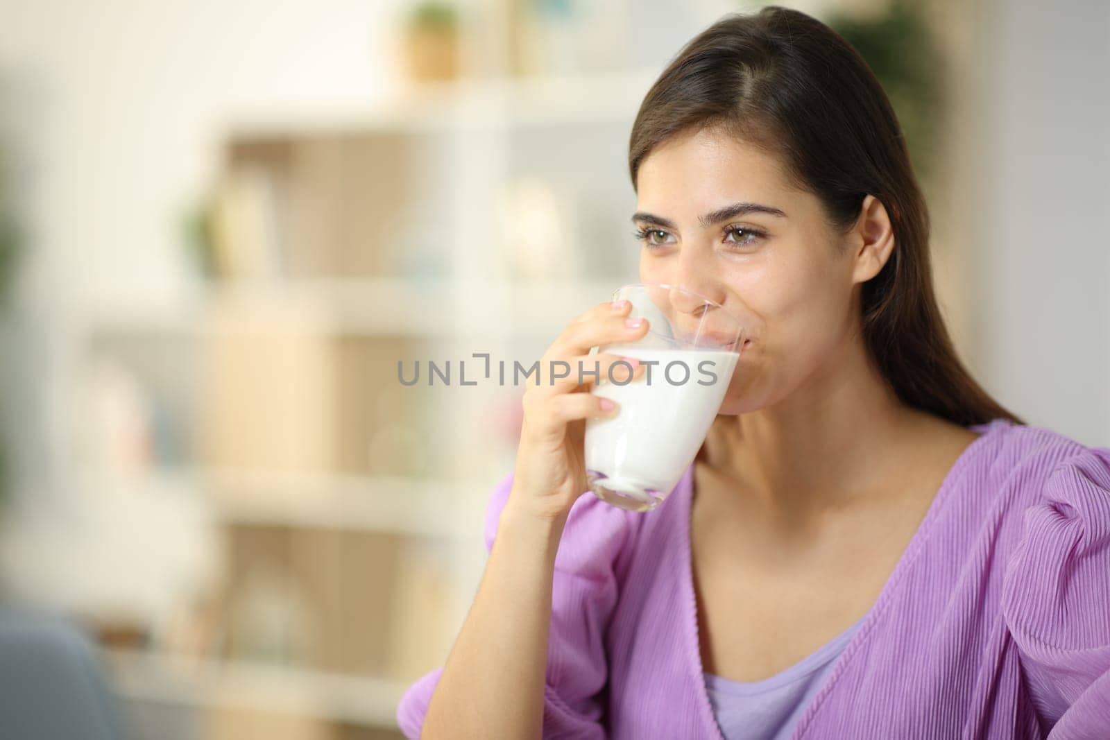 Happy woman drinking milk from glass looking away at home