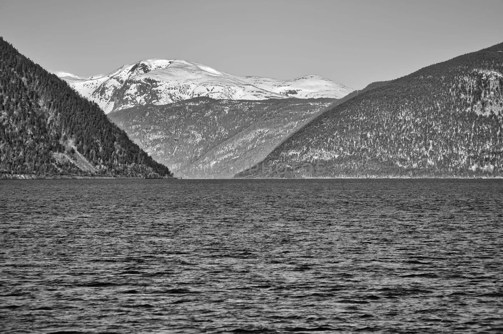 Norwegian fjord landscape in black and white. Blue water view of mountains with snow-covered peaks. Scandinavian nature from the north