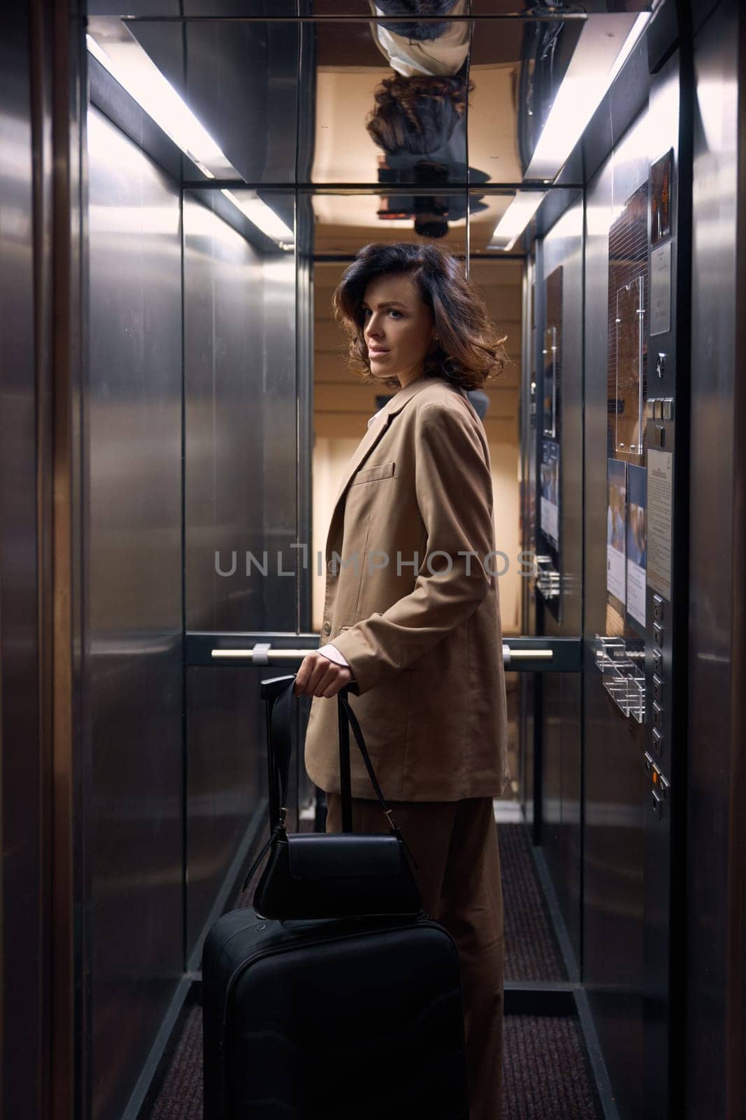 Elegant fashionable young businesswoman with luggage bags riding in hotel elevator arriving at place of destination. Business trip
