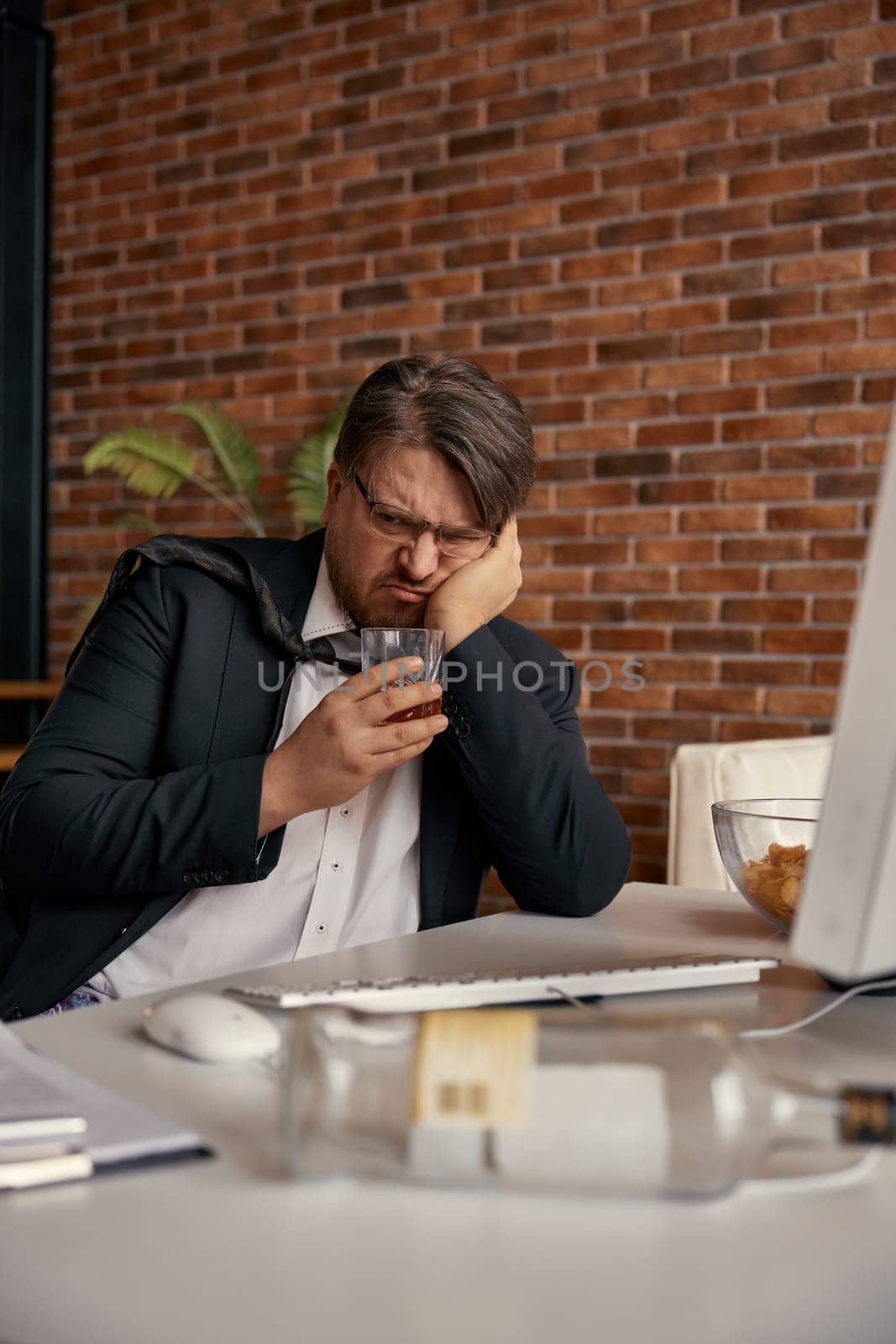Portrait of drunk businessman working online at virtual home office. Freelance job, stress and alcohol addiction concept
