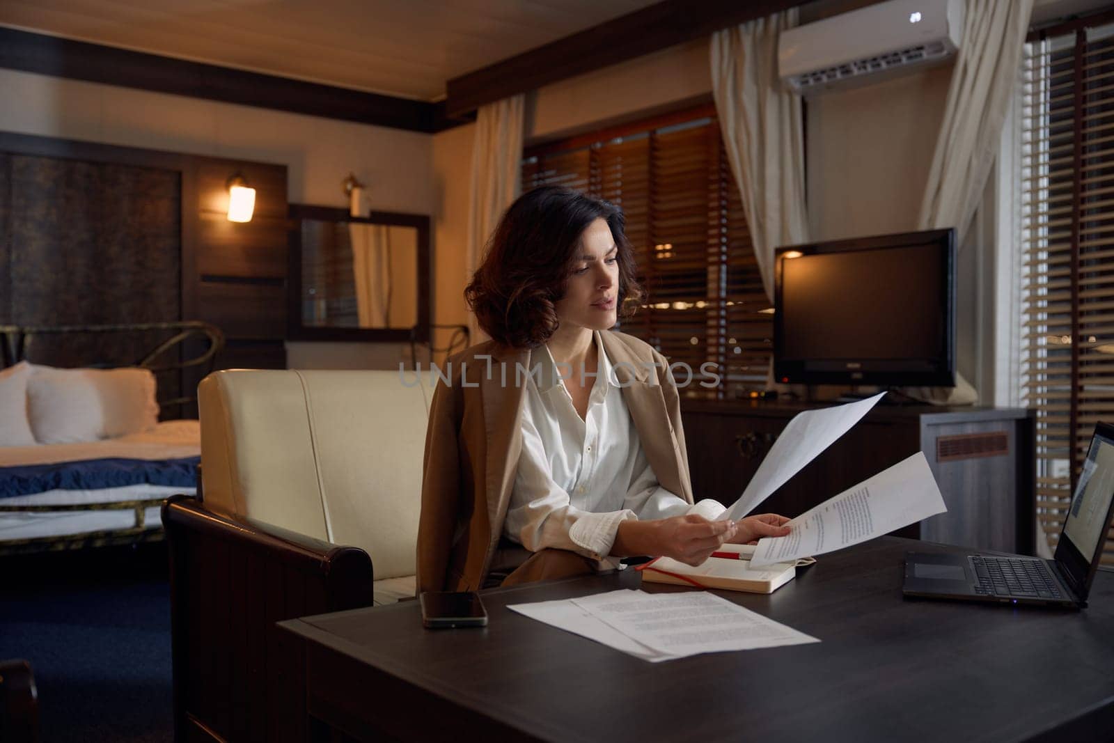 Businesswoman doing paperwork spending evening at hotel room. Business lady preparing for meeting or financial report at on-site conference abroad