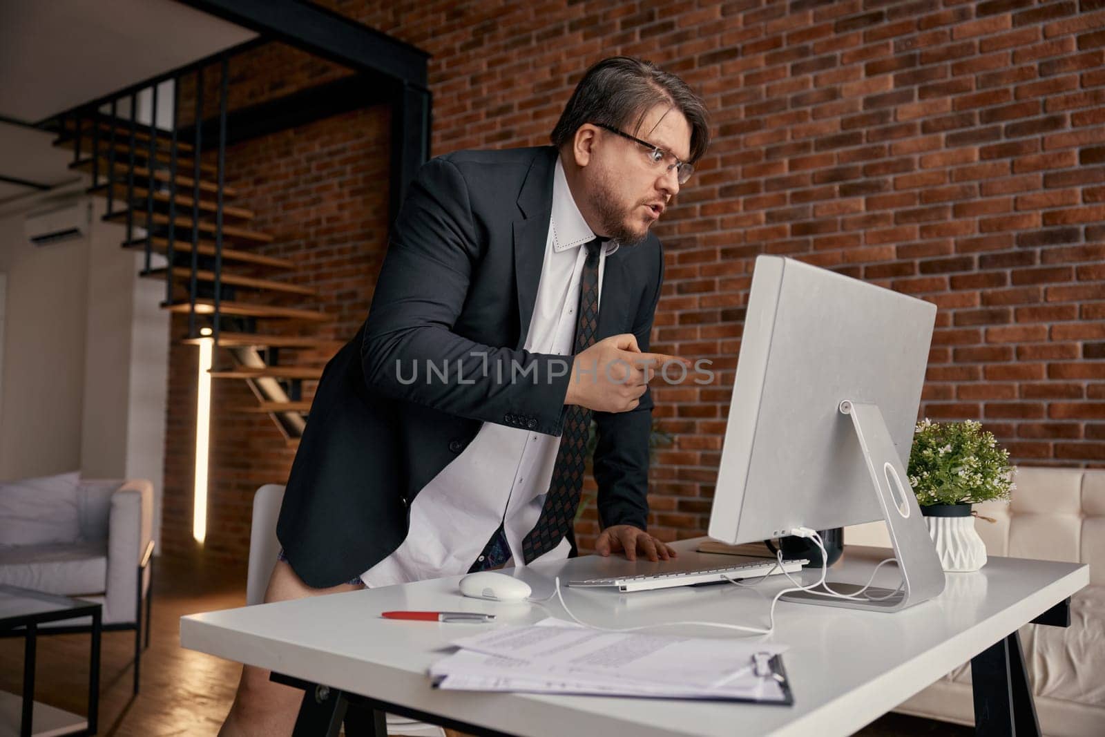 Mad furious businessman screaming loudly on computer screen while having online business meeting at home office. Remote job, videoconference, troubles at work, pc problems