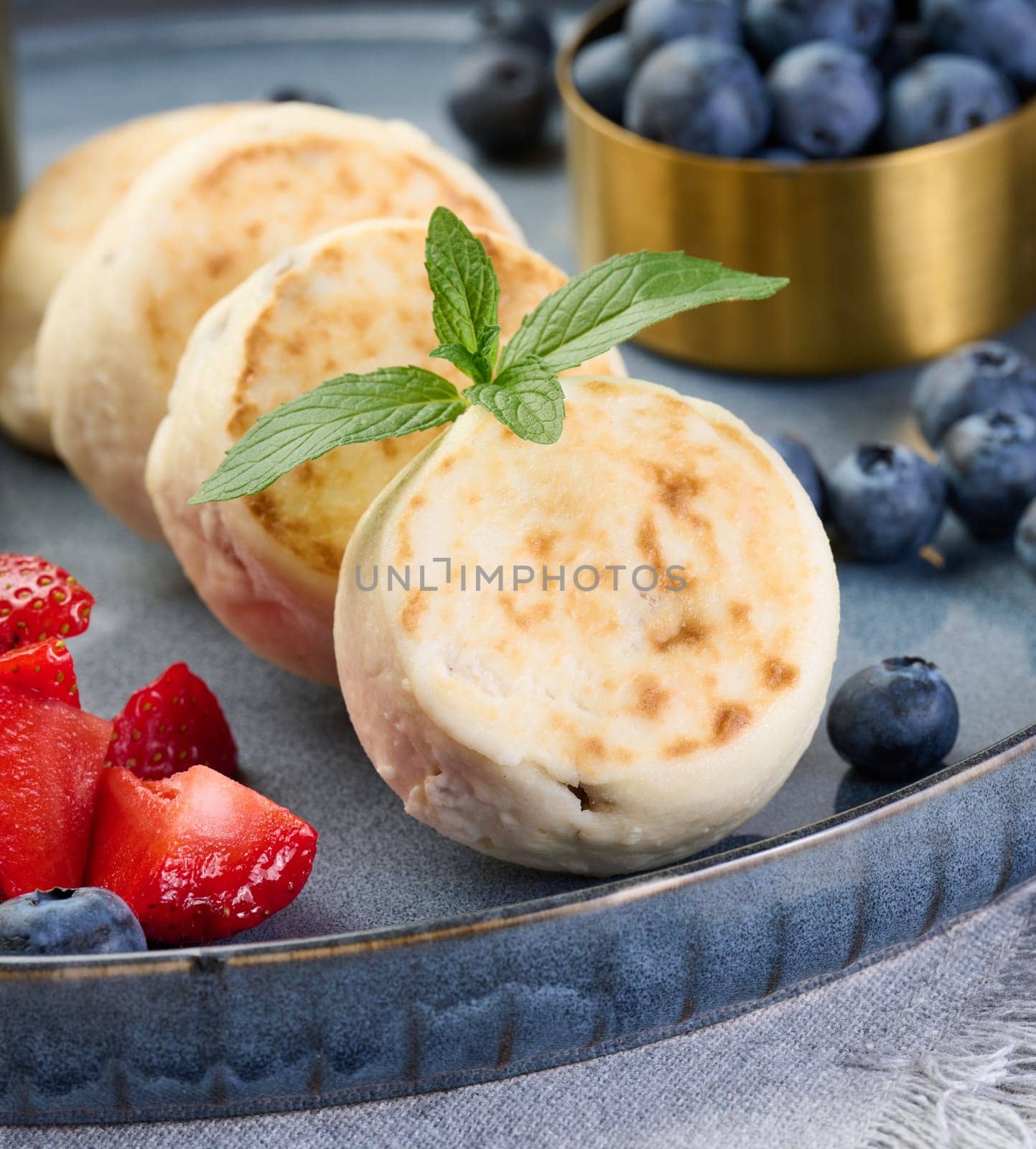 Round small fried cheesecakes on a blue plate with berries. Healthy breakfast