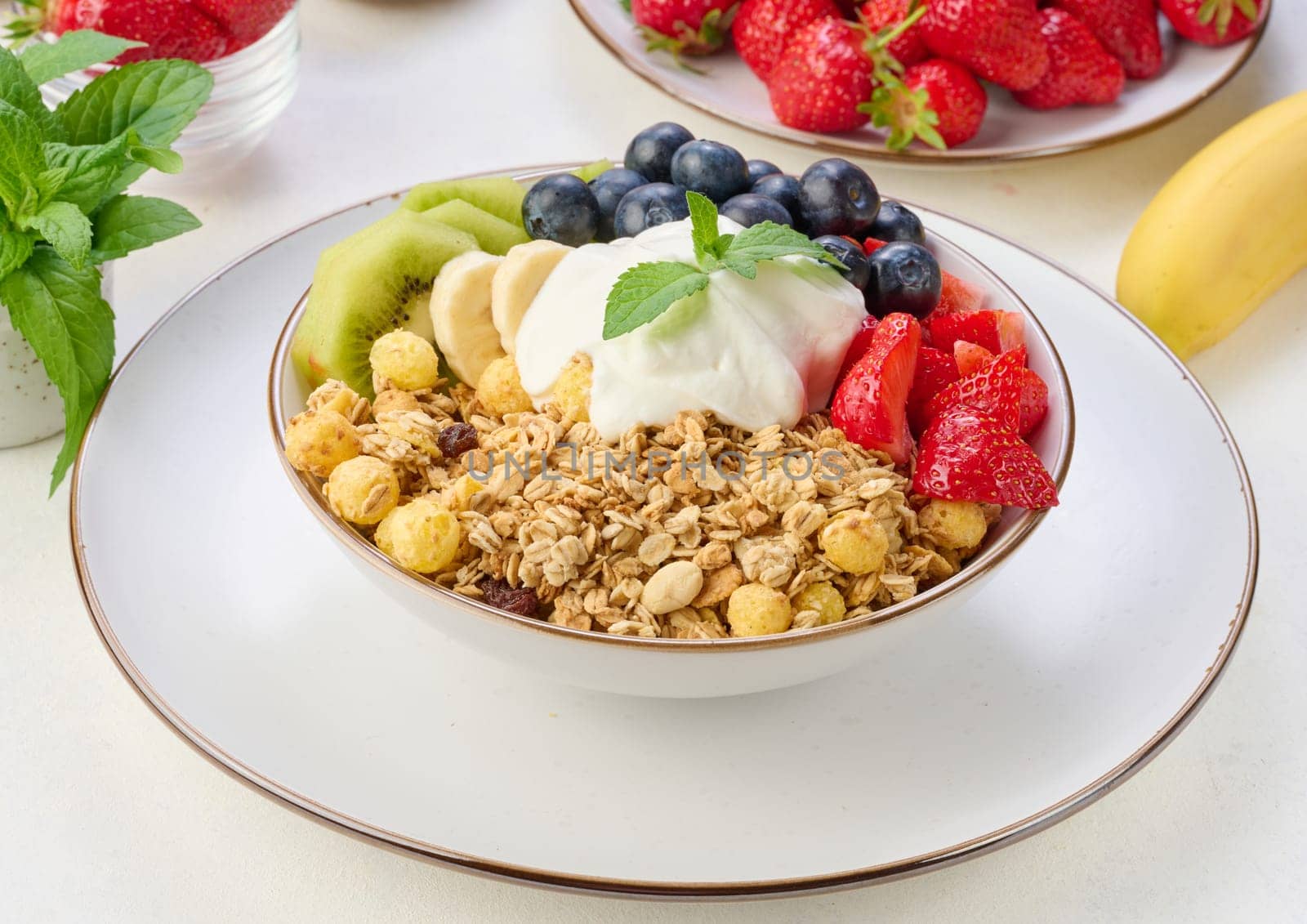 Granola with strawberries, kiwi, banana and blueberries in a round plate topped with yogurt on the table. Healthy and tasty food