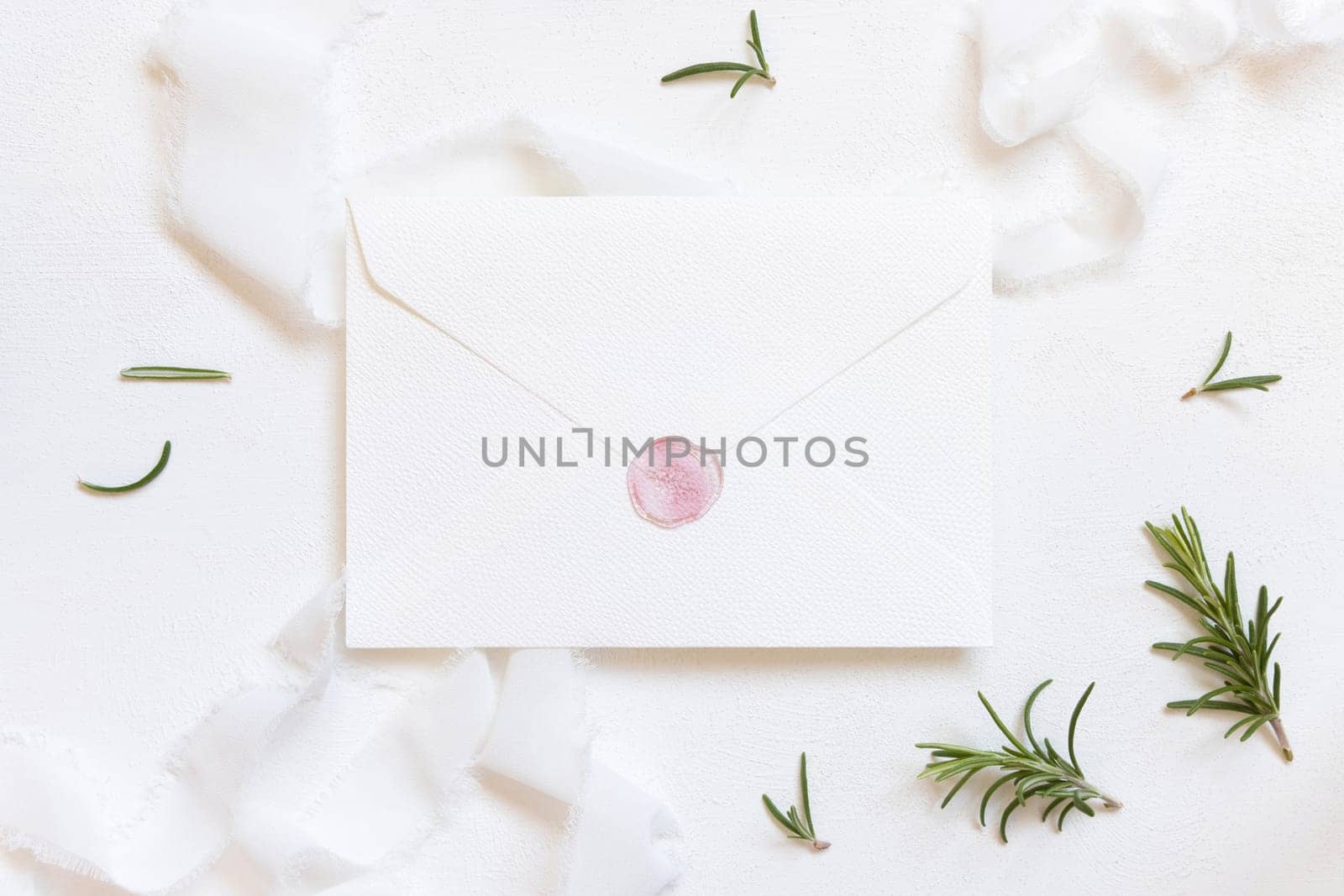 Blank sealed envelope near white silk ribbons and rosemary leaves top view, wedding mockup. Romantic scene with vertical cards and aromatic leaves flat lay. Valentines, Spring or Mothers day concept