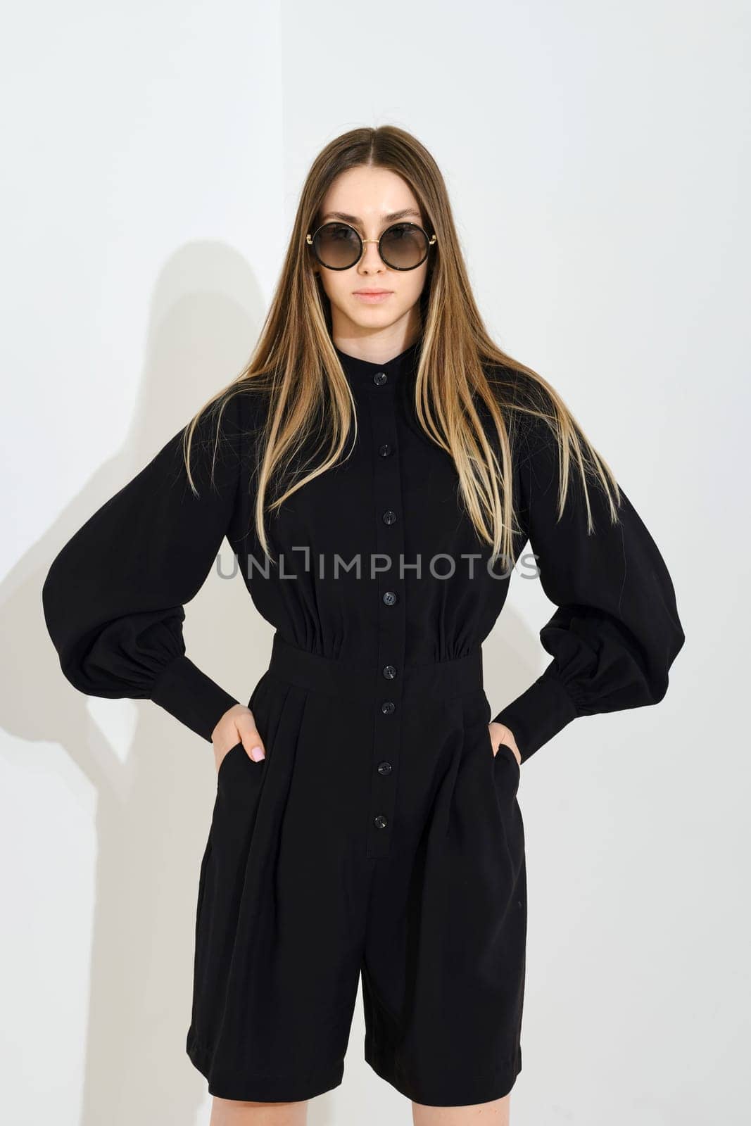 Young woman posing in black skort and blouse with loose sleeves over white background