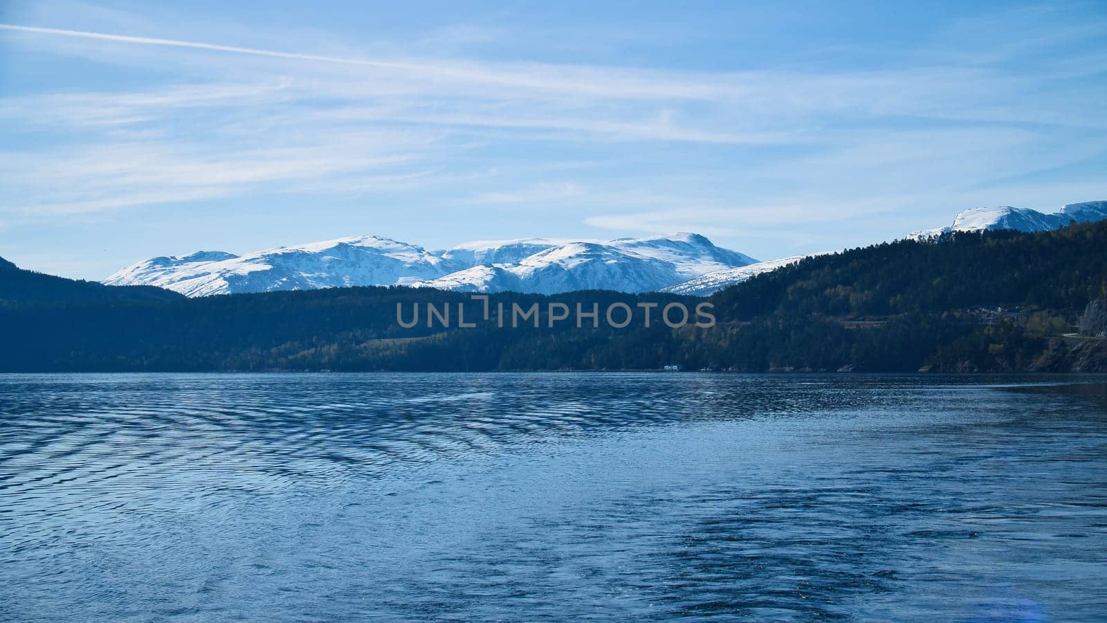 Norwegian fjord landscape. Blue water overlooking mountains with snow-covered peaks. Scandinavian nature from the north