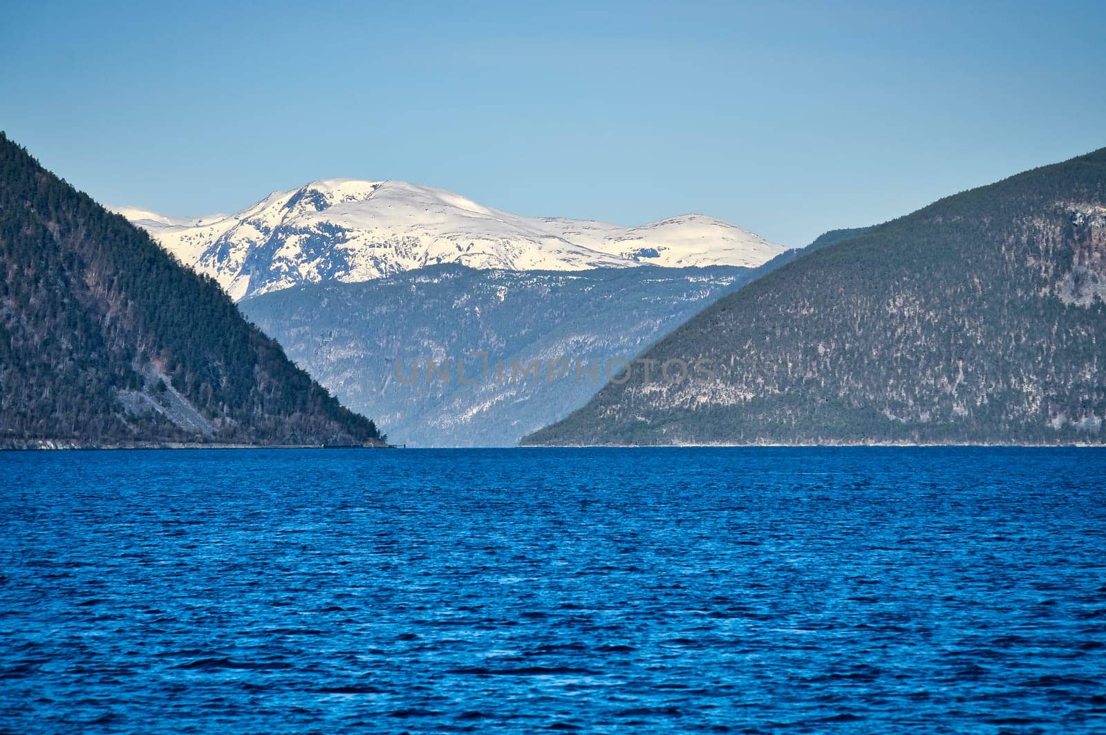Norwegian fjord landscape. Blue water overlooking mountains with snow-covered peaks. Scandinavian nature from the north