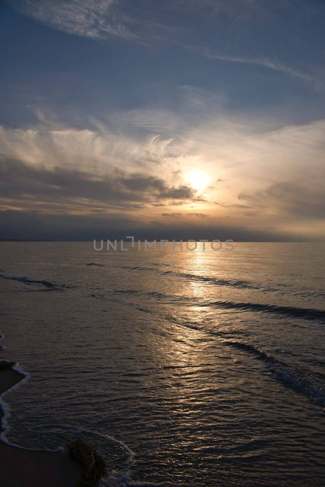 Sunset, illuminated sea. Sandy beach in the foreground. Light waves. Baltic Sea. Landscape on the coast