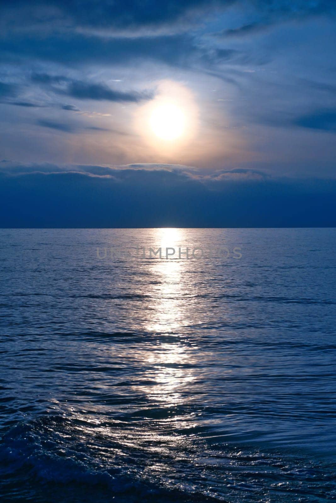Sunset, illuminated sea. A few clouds in the sky, light waves rolling onto the Baltic Sea beach. Landscape on the coast