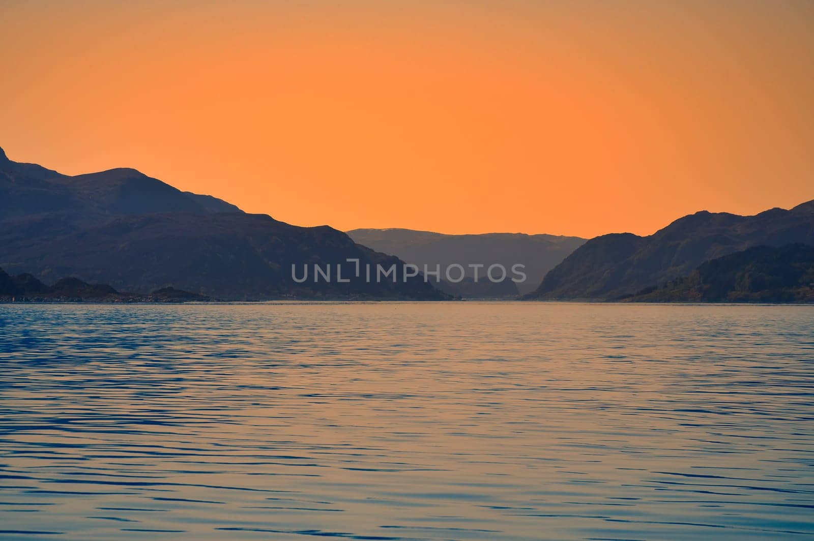 Norwegian fjord landscape at dusk. View of snow-capped mountains with rugged vegetation. Crystal clear water in the foreground. Landscape from Scandinavia
