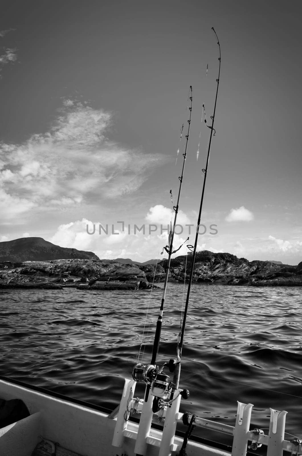 Fishing boat with fishing rod off mountains in the Norwegian fjord landscape in black and white. Crystal clear water in Scandinavia