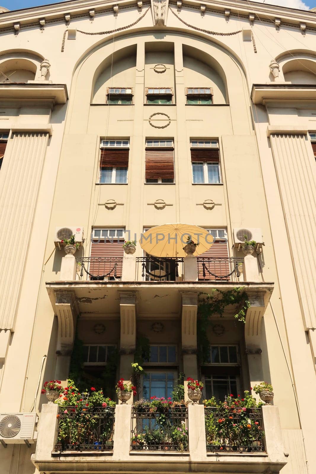 Beautiful balconies with green plants and an umbrella on the facade of a high neoclassical house, building close to the Knez Mihailova, Knez Mihaila Street in the city center of Belgrade, Serbia 2022