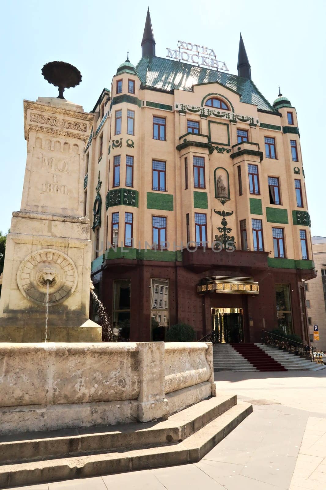The Terazije drinking fountain next to the front facade of the Hotel Moskva, Palace Rossiya, which is an example of Art Nouveau architecture in the city center of Belgrade, Serbia 2022