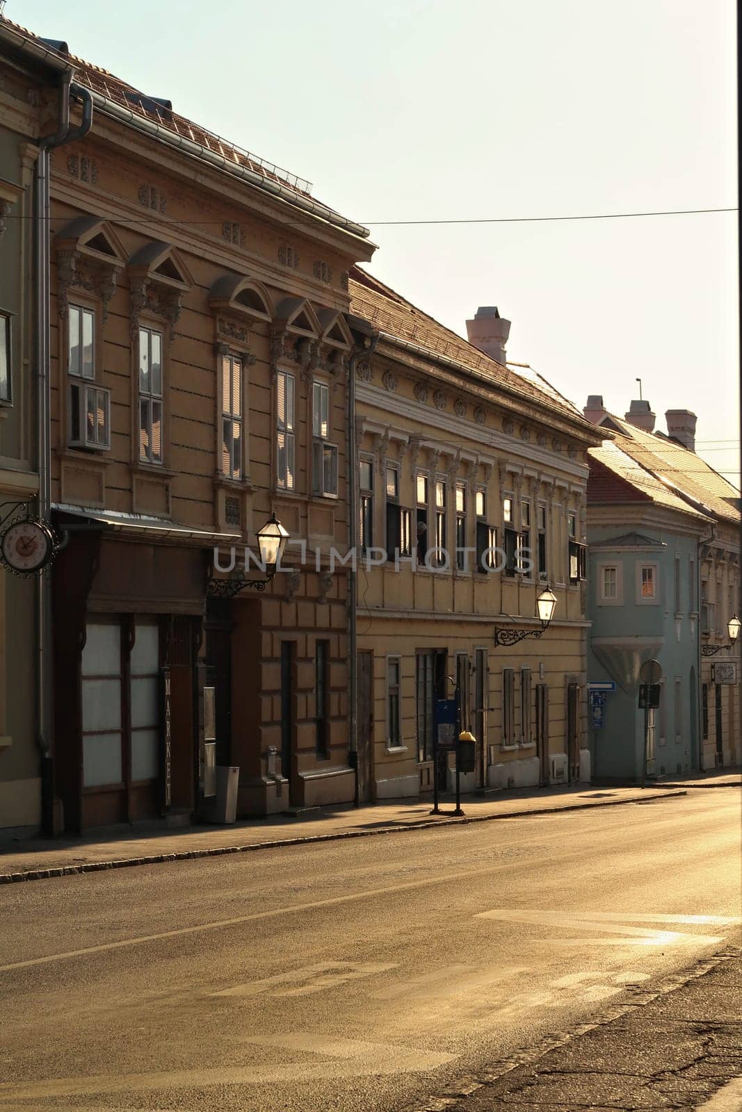 Golden hour inside the Petrovaradin Lower Fortress, sunlight is shining through the street lamps, lanterns on the facades of historic buildings and reflecting on the windows, Novi Sad, Serbia 2022