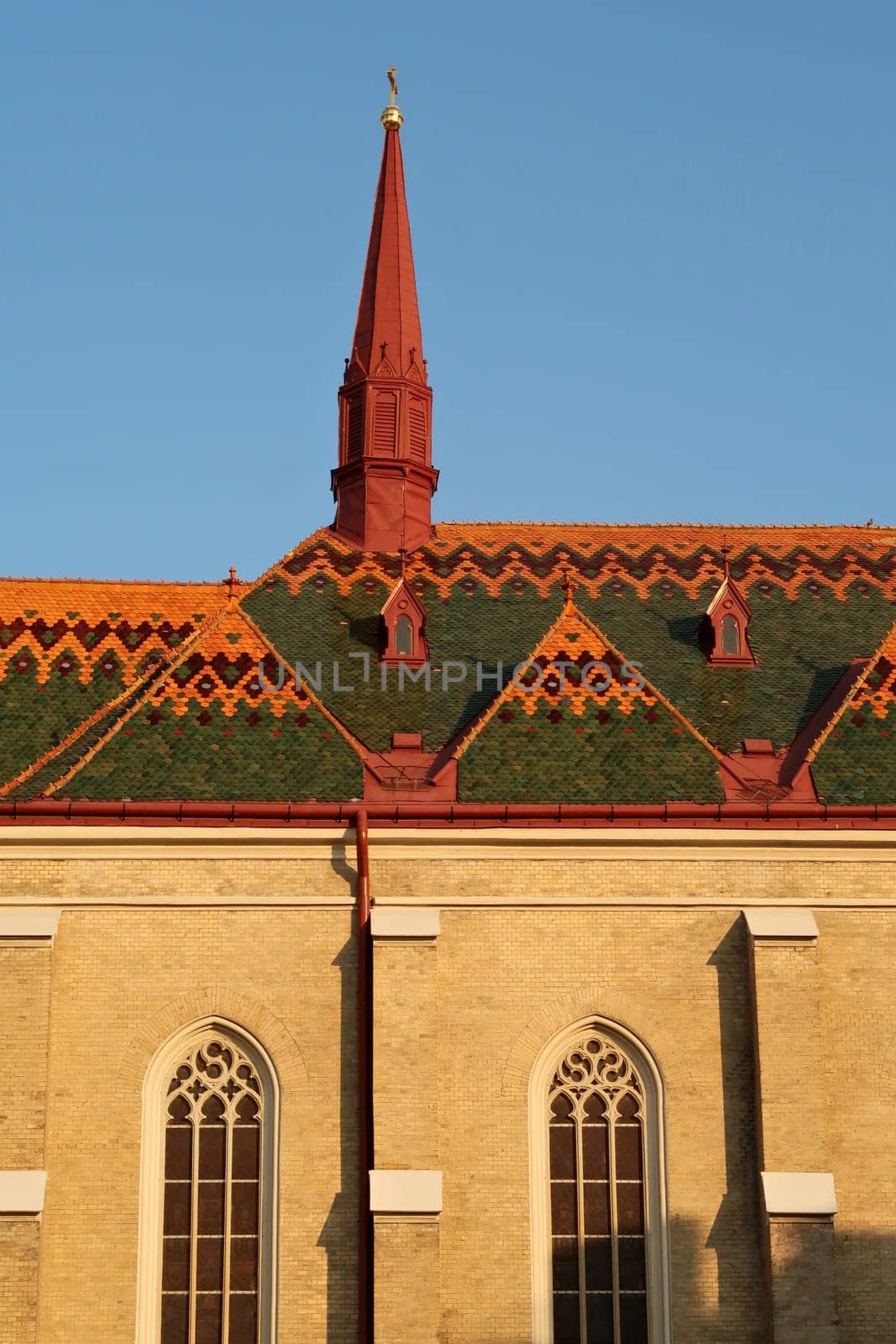Side facade with stained glass windows and colorful roof with little red tower of the Name of Mary Church in the city center, old town of Novi Sad, Serbia 2022