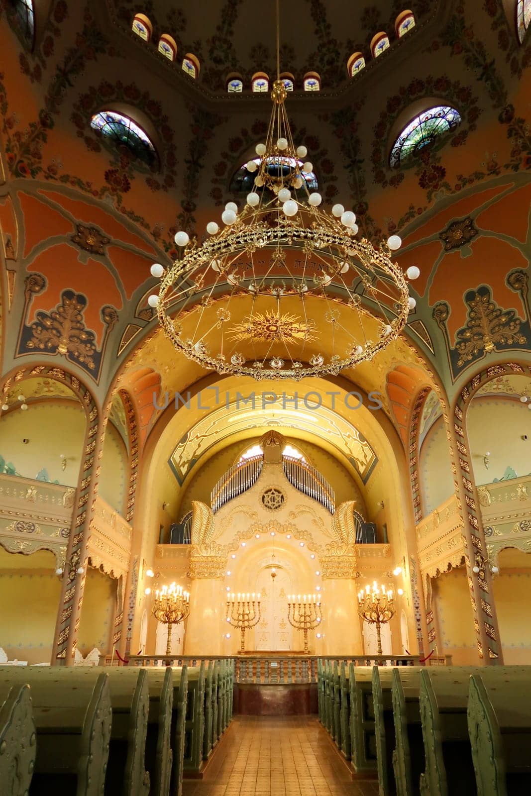 Inside the Synagogue of Subotica, a big golden chandelier is hanging from the colorful ceiling over the the benches and the aisle leading to the altar, Subotica, Serbia 2022