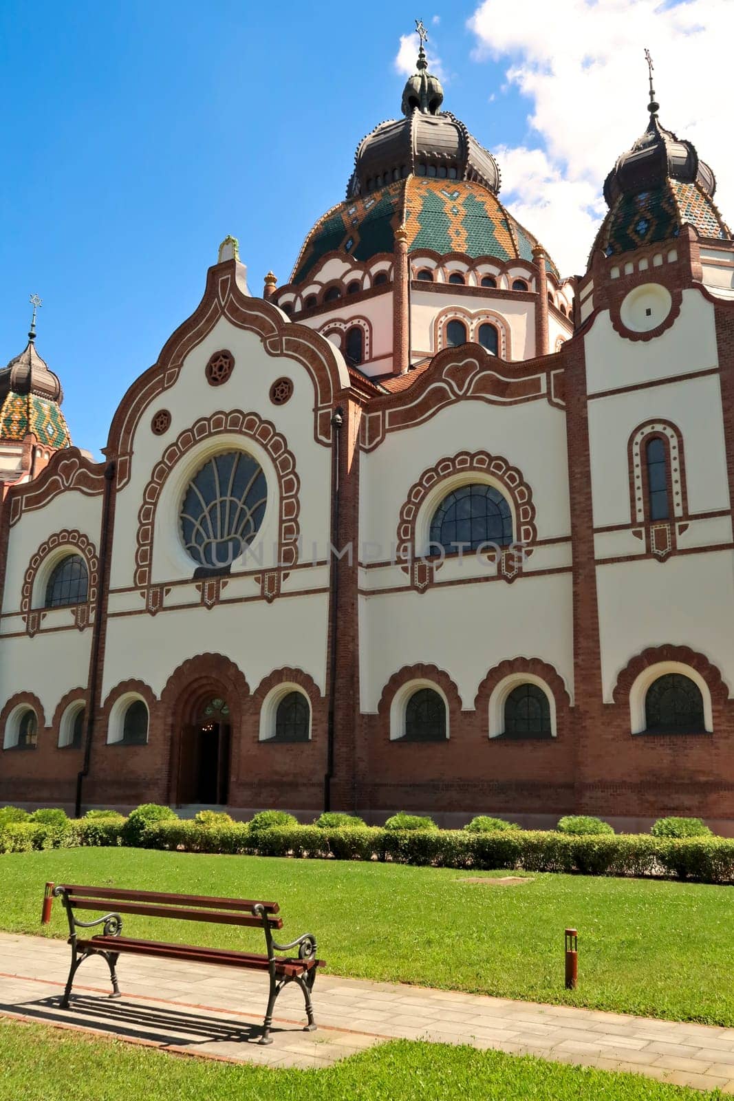 The side entrance and facade of the Synagogue of Subotica on a sunny day with a little bench in the foreground, Subotica, Serbia 2022