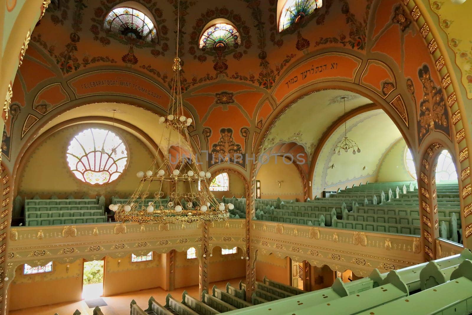 Inside the Synagogue of Subotica, the big golden chandelier is hanging from the painted ceiling surrounded by galleries filled with benches, Subotica, Serbia 2022