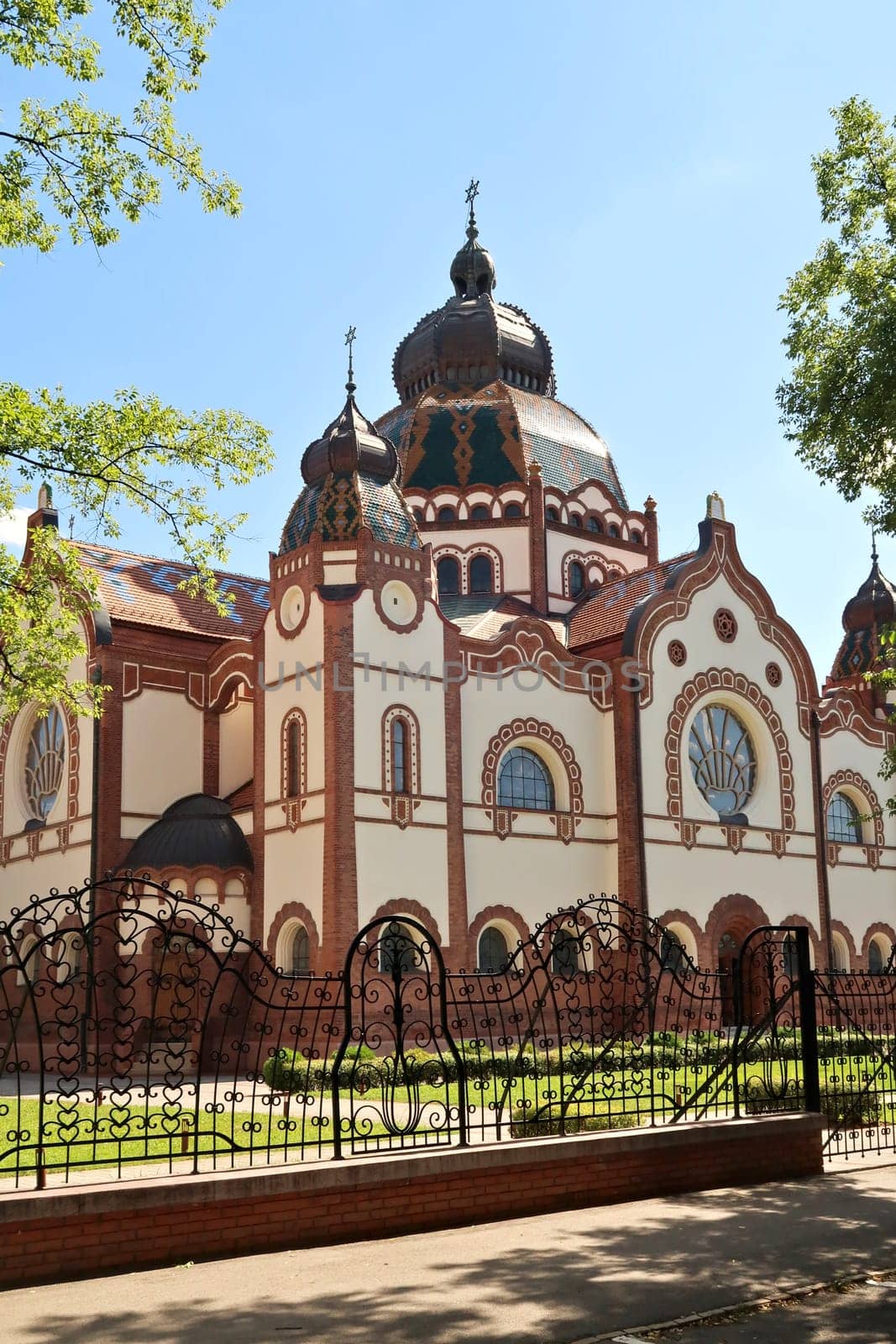 The Synagogue of Subotica behind a black metal fence with elaborate details on a sunny day, Subotica, Serbia 2022