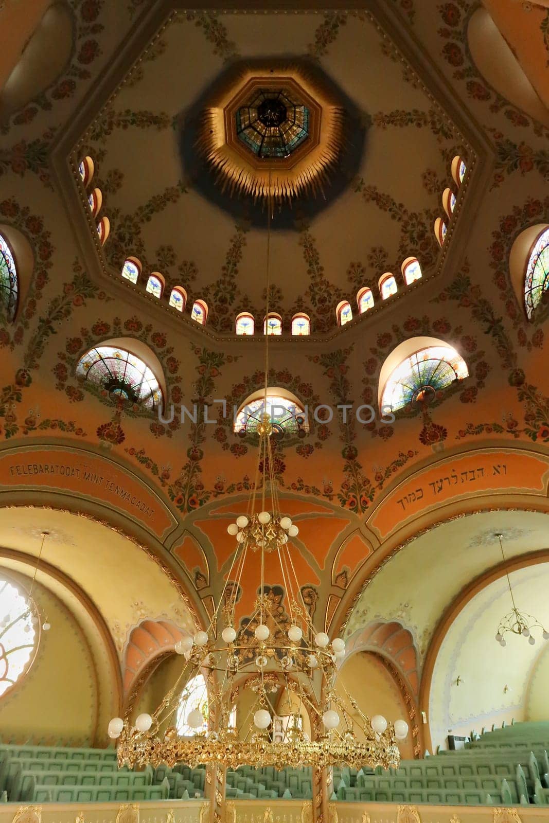 Inside the Synagogue of Subotica, the big golden chandelier is hanging from the painted ceiling, vault, dome, light is shining through stained glass windows, Subotica, Serbia 2022