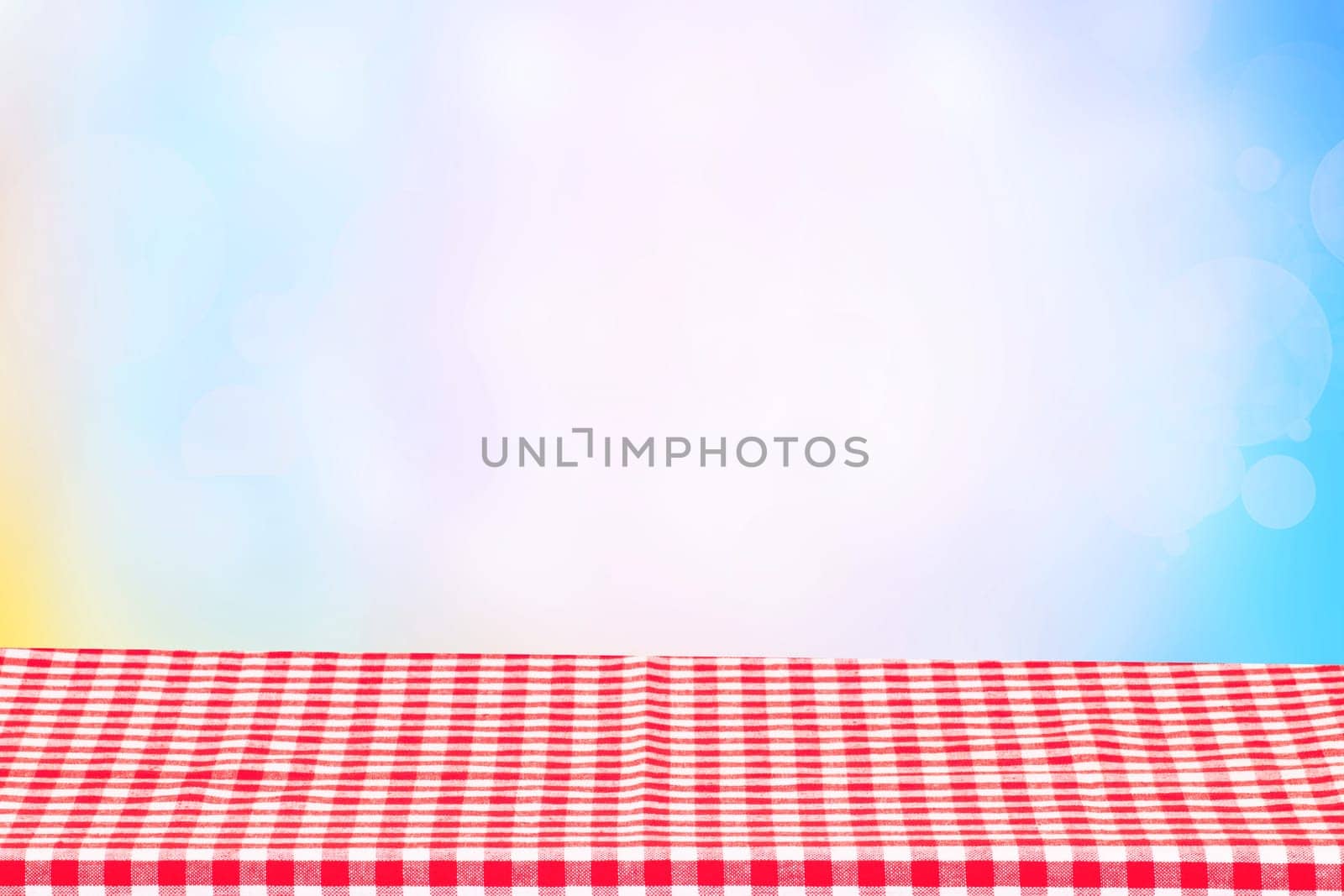 Empty table product. Empty colorful checkered tablecloth over abstract blurred natural spring background texture with space for your food and product display montage.